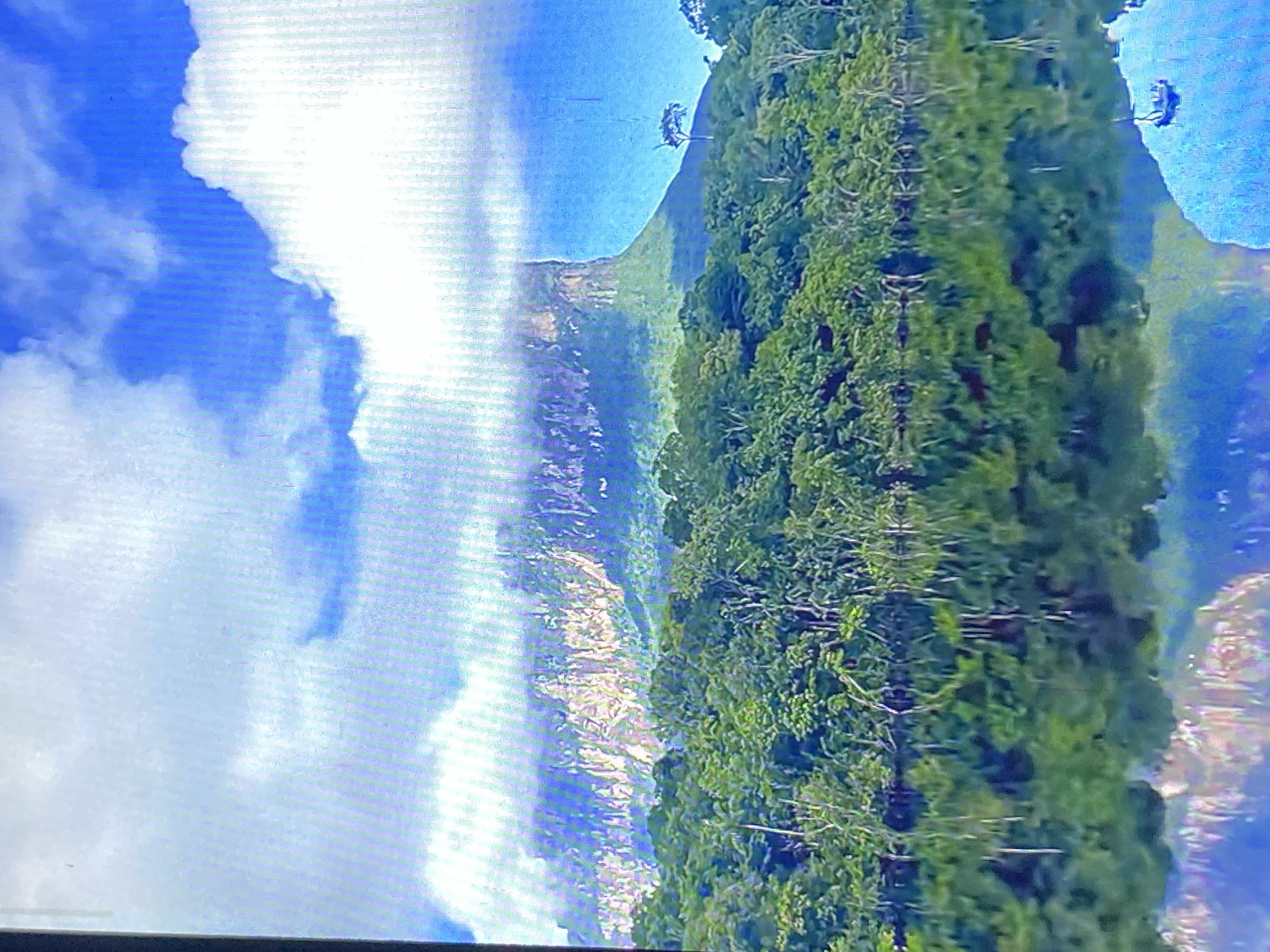 The image shows a landscape, likely in a mountainous region. The sky is blue with white clouds. A mountain with a bare, rocky face is visible. To the right of the mountain, there is a dense forest with green trees. The image appears to be a photograph of a natural landscape, and the location is believed to be in Tinaquillo, Venezuela.
