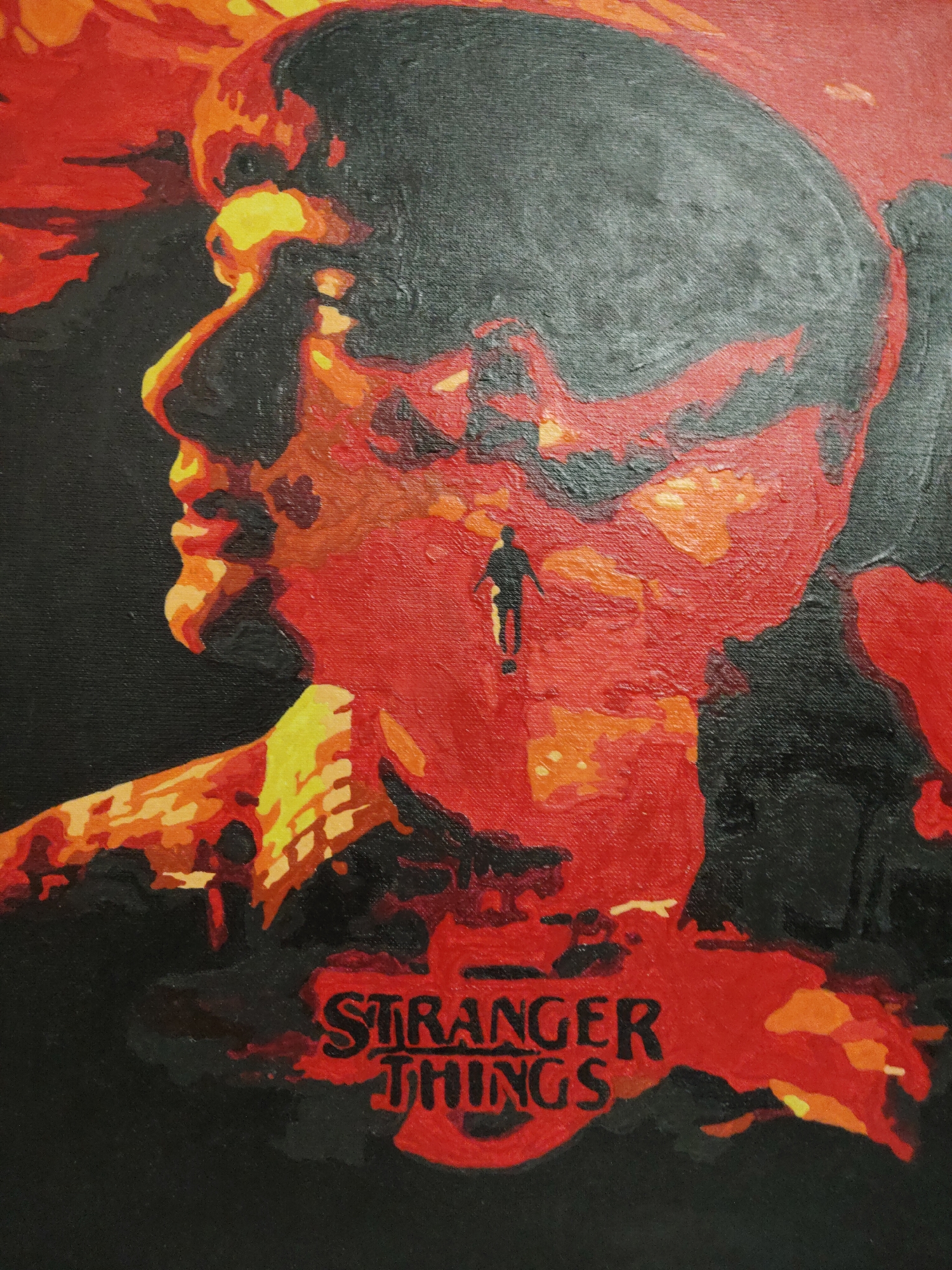 An acrylic painting on canvas depicts a striking and surreal portrait, dominated by a large, abstract profile of a human head and upper torso, facing left. The profile is rendered in vibrant shades of red, orange, and yellow, creating a fiery or molten appearance, set against a stark black background. These warm colors form the contours and internal details of the face, suggesting a landscape or an inner world.
Within the red-orange expanse near the larger profile's ear and neck, a small, silhouetted figure of a person is visible, walking or standing. This tiny figure provides a sense of scale and adds a narrative element of exploration within the abstract landscape of the main subject. The texture of the canvas and visible brushstrokes are evident throughout the artwork, giving it a tactile quality.
At the bottom center of the painting, the words "STRANGER THINGS" are distinctly displayed in black lettering against a red background, using the iconic typeface associated with the television series. The overall color palette of black, red, orange, and yellow evokes themes often present in the show, such as danger, the Upside Down, or intense emotional states. The composition is reminiscent of a stylized poster or graphic art, blending human form with abstract, atmospheric elements.
