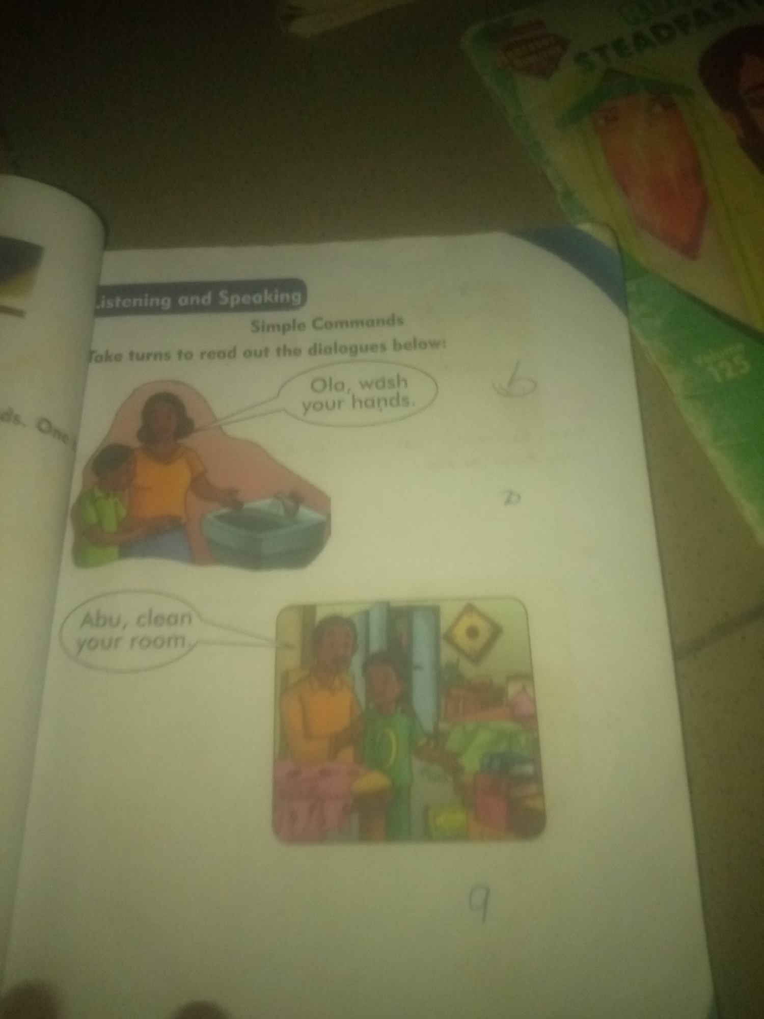 The image depicts a page from a children's educational book, likely for early language learning. The page is titled "Listening and Speaking" and features a section on "Simple Commands." Below the title, there is an instruction to "Take turns to read out the dialogues below."
The page contains two illustrations with accompanying text bubbles, illustrating simple commands.
The first illustration shows a woman and a young boy standing next to a sink. The woman, wearing an orange shirt, is pointing towards the sink. The boy, in a green shirt, is looking towards the sink. A text bubble above them reads: "Ola, wash your hands." The style of illustration is simple and cartoon-like, typical for children's books.
The second illustration depicts a domestic scene with a man and a young boy. The man, in an orange shirt, is facing away from the viewer, while the boy, in a green shirt, is looking towards the viewer. The room appears to be a bedroom, with a bed and toys visible in the background. A text bubble connected to this illustration reads: "Abu, clean your room." This illustration also uses a simple, cartoonish style.
There are also some handwritten markings on the page, including the letter "b" and the letter "d" in what appears to be a faded blue or grey ink, as well as a handwritten "q" in black ink.
The overall environment appears to be an indoor setting, likely a classroom or a home where the book is being used. The background of the page is off-white, and the lighting suggests it is not a brightly lit environment.
There is no information in the image to suggest its location in the city of Jalingo, Nigeria.
