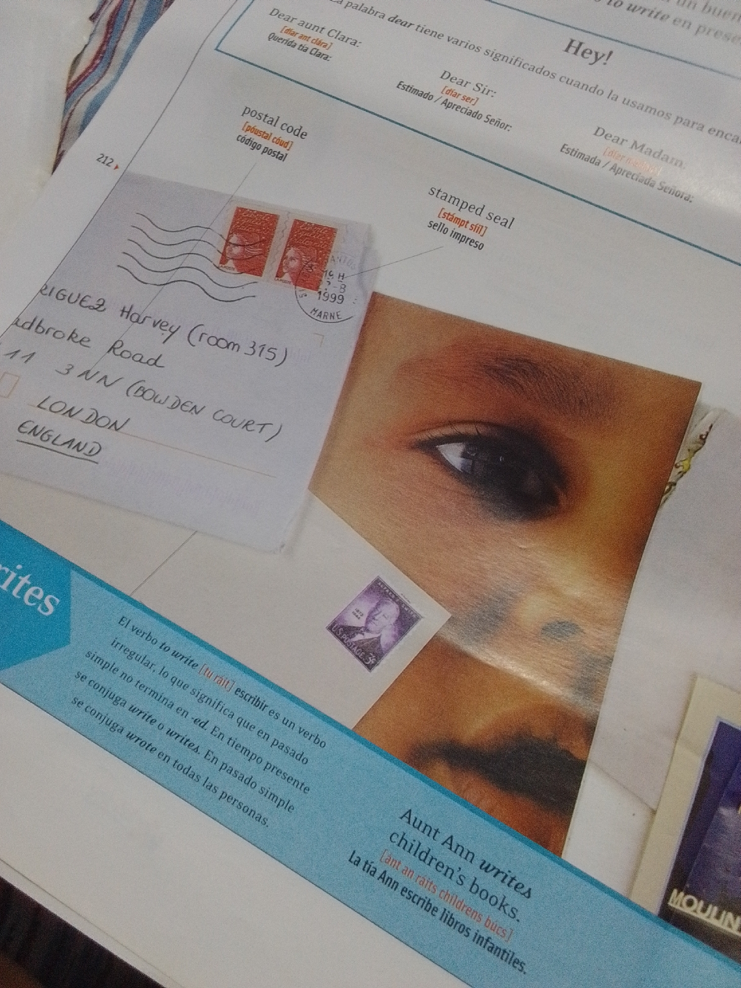 The image shows a page from a book or educational material, featuring text and visual elements related to letter writing. In the foreground, a portion of an envelope is visible with handwriting that appears to be an address. Two postage stamps are affixed to the envelope. To the right, there is a photograph of a child's eye and upper face, partially obscured by the book page. Text in English and Spanish is present on the page, including phrases like "Dear Aunt Clara," "postal code," and "stamped seal." The bottom of the image shows a blue section with text discussing the verb "to write." There is no discernible information or visual cue within this image that relates to the city of La Tagua, Venezuela.