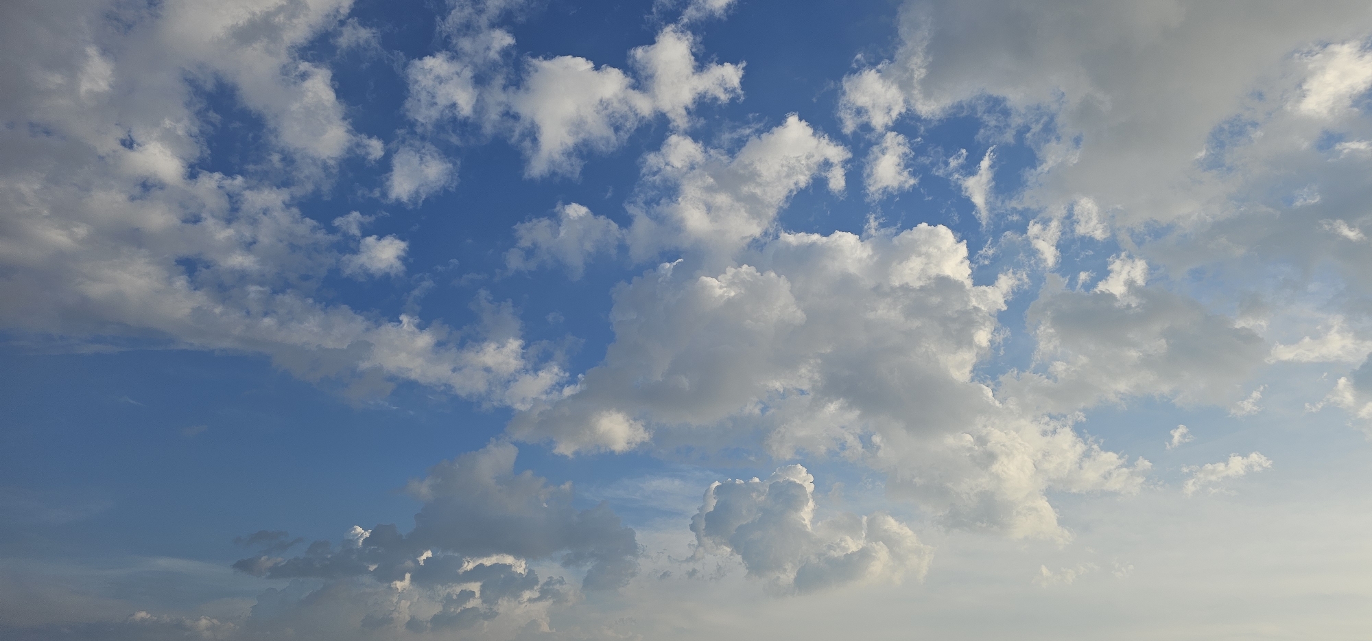 The image is a landscape photograph of a sky filled with clouds. The sky is a vibrant blue, with scattered white and gray clouds. Some clouds are puffy and cumulus-like, while others are wispy and cirrus-like. The light suggests it might be late afternoon or early morning, as there is a soft, diffused quality to the light. There are no people, structures, or any specific landmarks visible that would indicate a location within the city of Makati, Philippines. The scene is purely focused on the natural phenomenon of the sky and clouds.