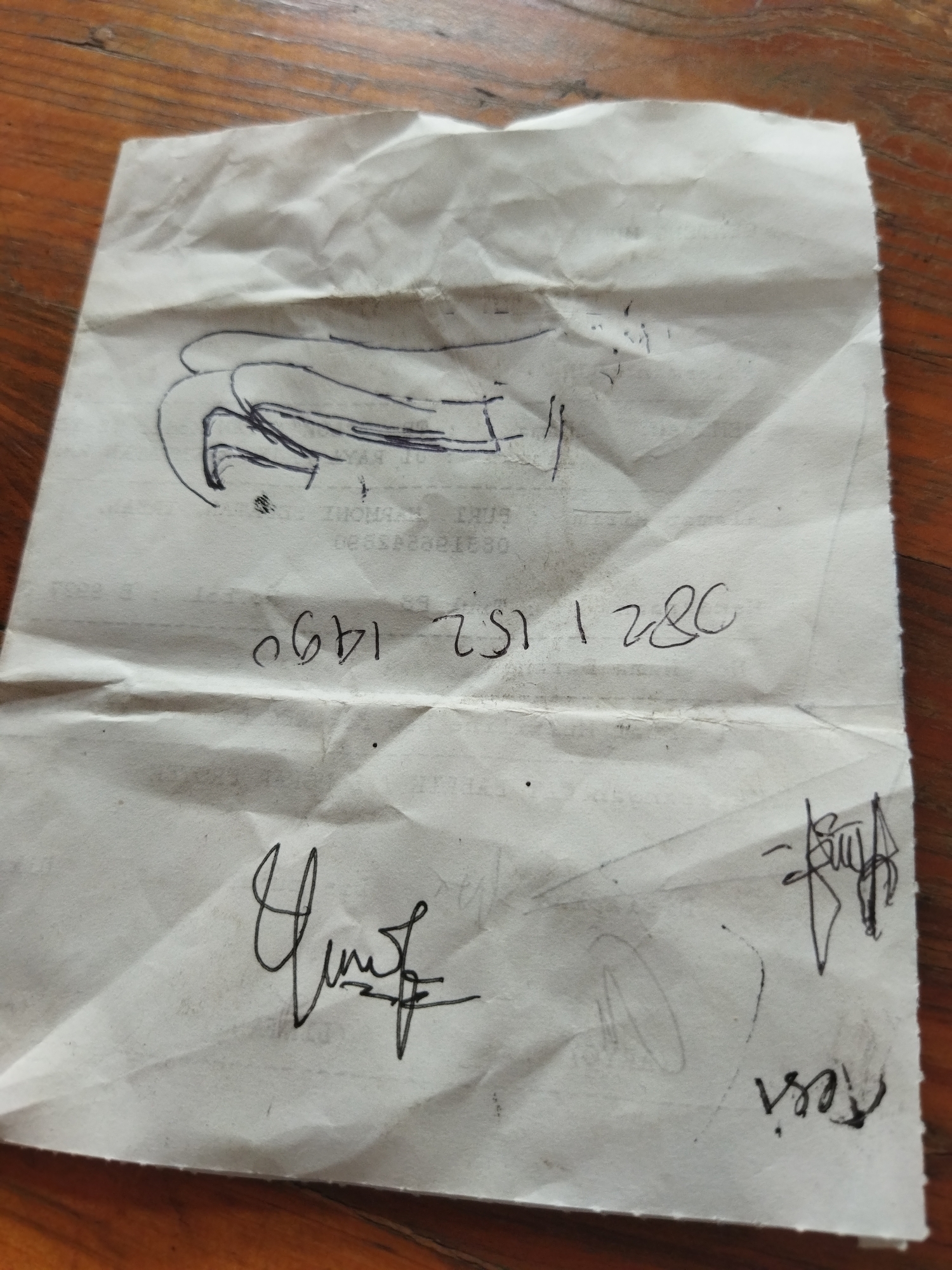 The image shows a crumpled piece of paper on a wooden surface. The paper has handwritten text and drawings. In the top section, there is a crude drawing of a hand or a large object. Below the drawing, there are some faint lines of text. In the middle section, there is a handwritten number "0691 1490 280". The bottom section has two signatures or handwritten names, one on the left and one on the right. The signature on the left appears to be more elaborate, while the one on the right is smaller and appears to say "resi". The overall impression is of a hastily scribbled note. The location of Suka Sari, Indonesia, is not visible in the image.