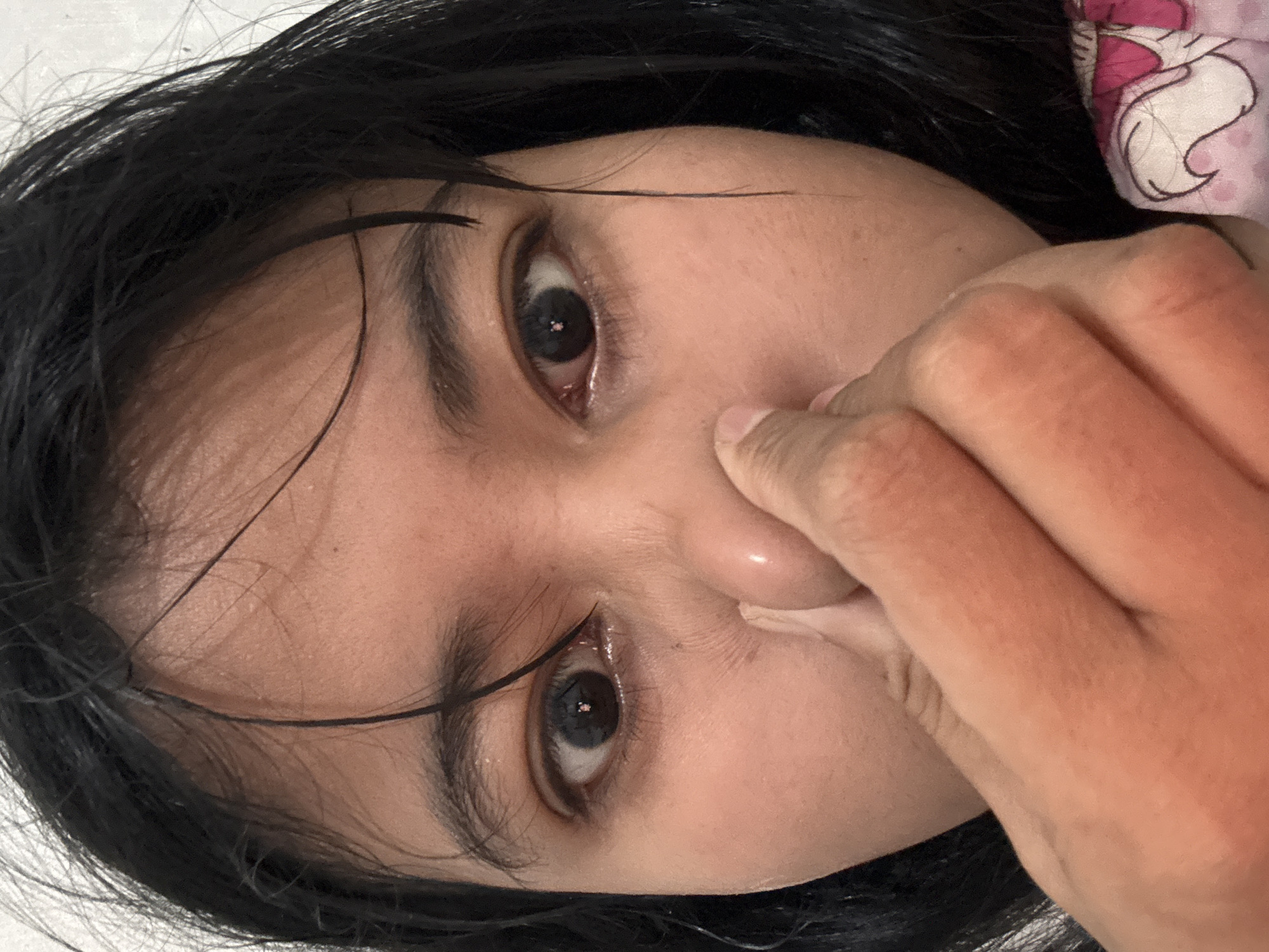 A close-up, head-on shot shows a person's face, with a hand covering their nose and mouth. The individual has dark hair and dark eyes, with visible eyelashes. Their skin appears to be light brown. The background is a plain, off-white color. The image is a still photograph and does not depict any specific location in North Jakarta, Indonesia.