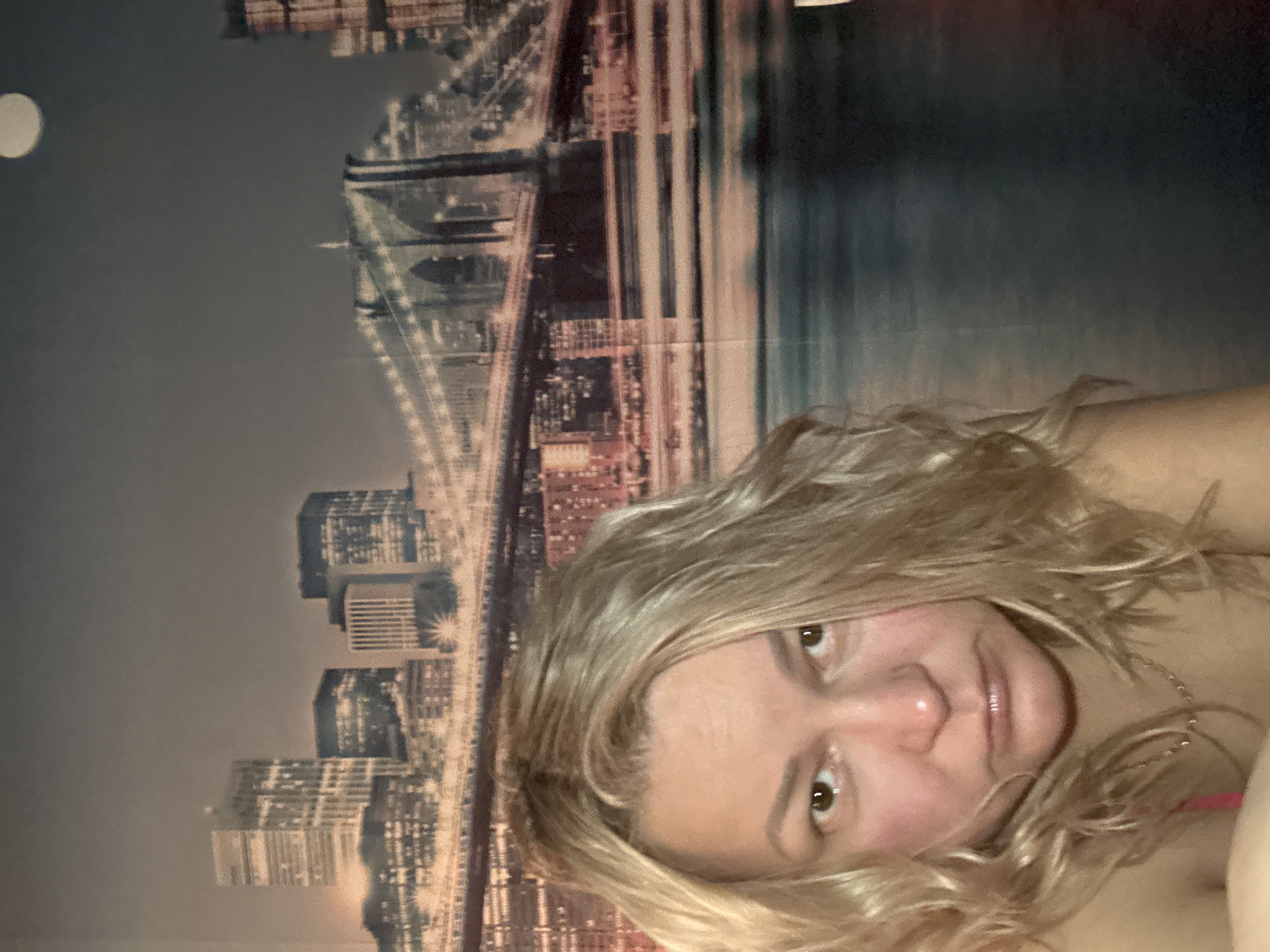 A woman with blonde hair is in the foreground. Behind her is a depiction of a city skyline with a bridge and several buildings. A bright circle is visible at the top left, potentially representing the moon. The image is oriented sideways. There is no indication of Русский Вожой, Russia.