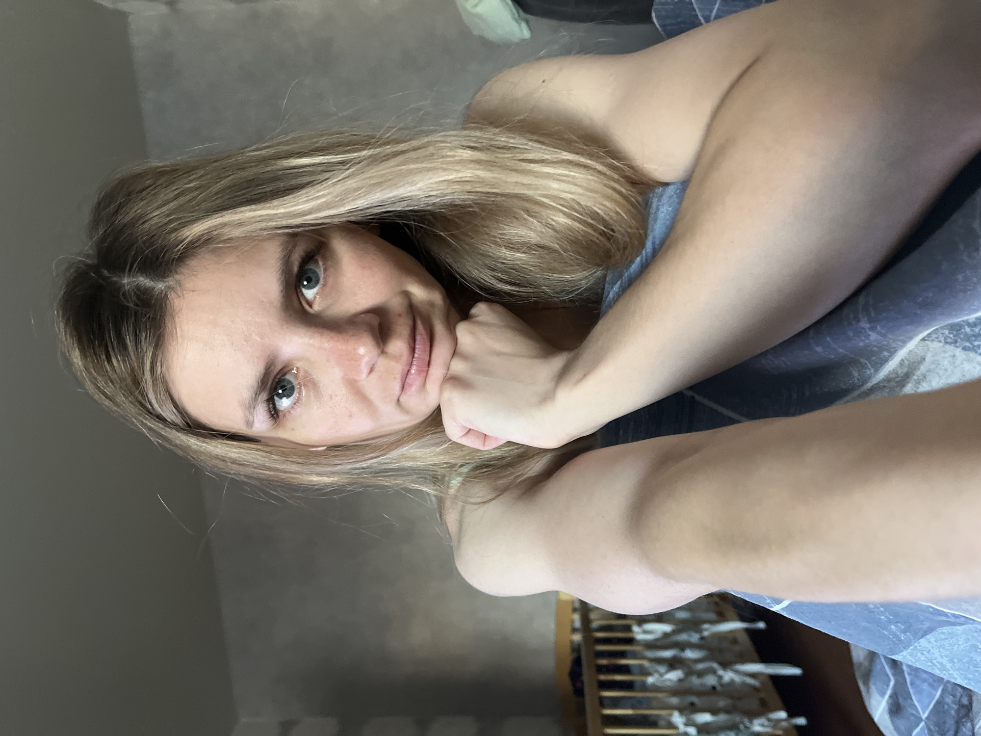 A woman with blonde hair is lying on a bed and resting her head on her hand. The location cannot be determined with the given information.