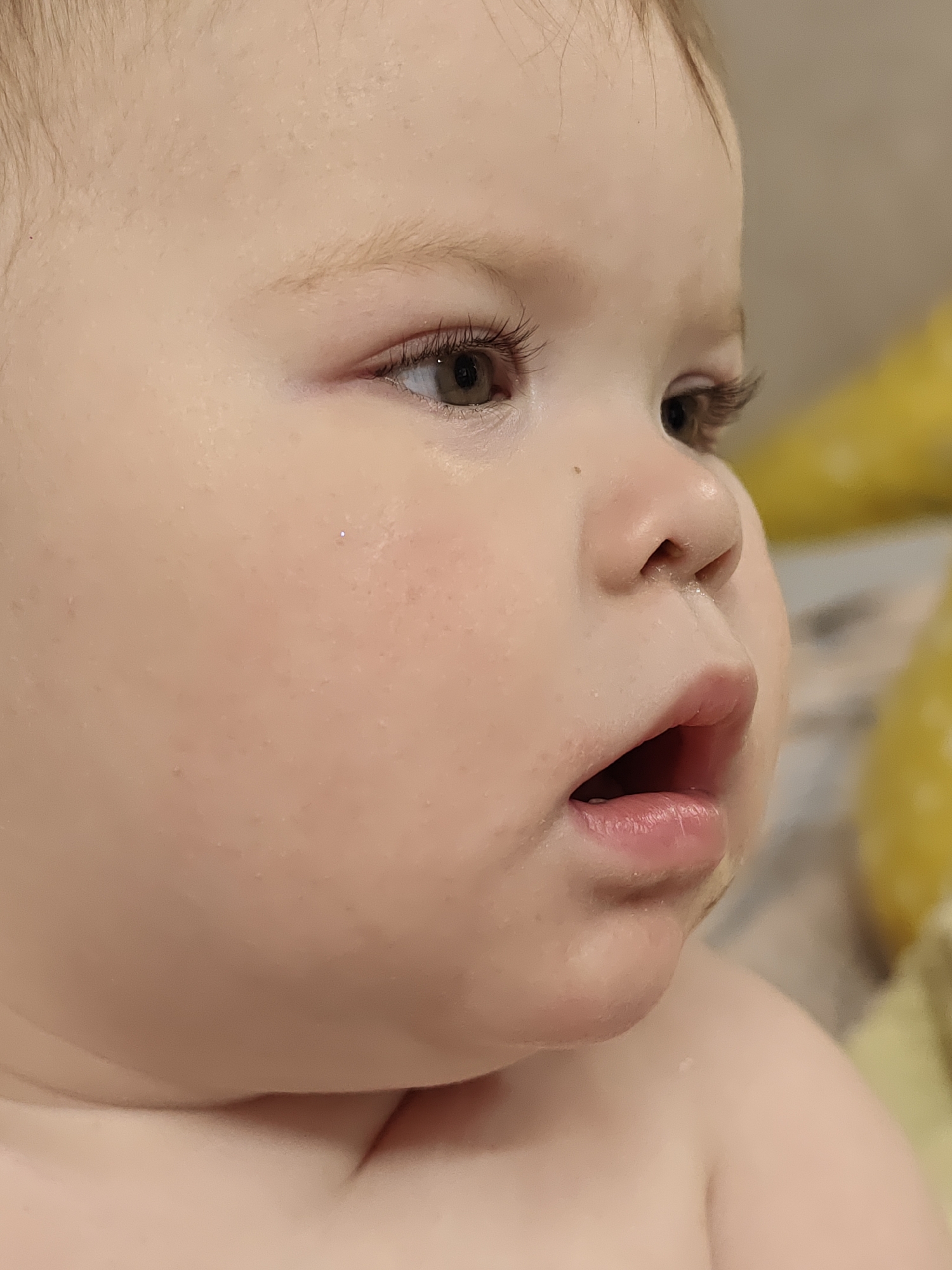 A close-up, side-view shot depicts a young child with fair skin and light brown hair. The child's face is partially wet. The child has an open mouth and slightly runny nose. The background is blurry and indistinct, with some yellow hues. The image does not contain any information related to the city of Chaikovsky, Russia.