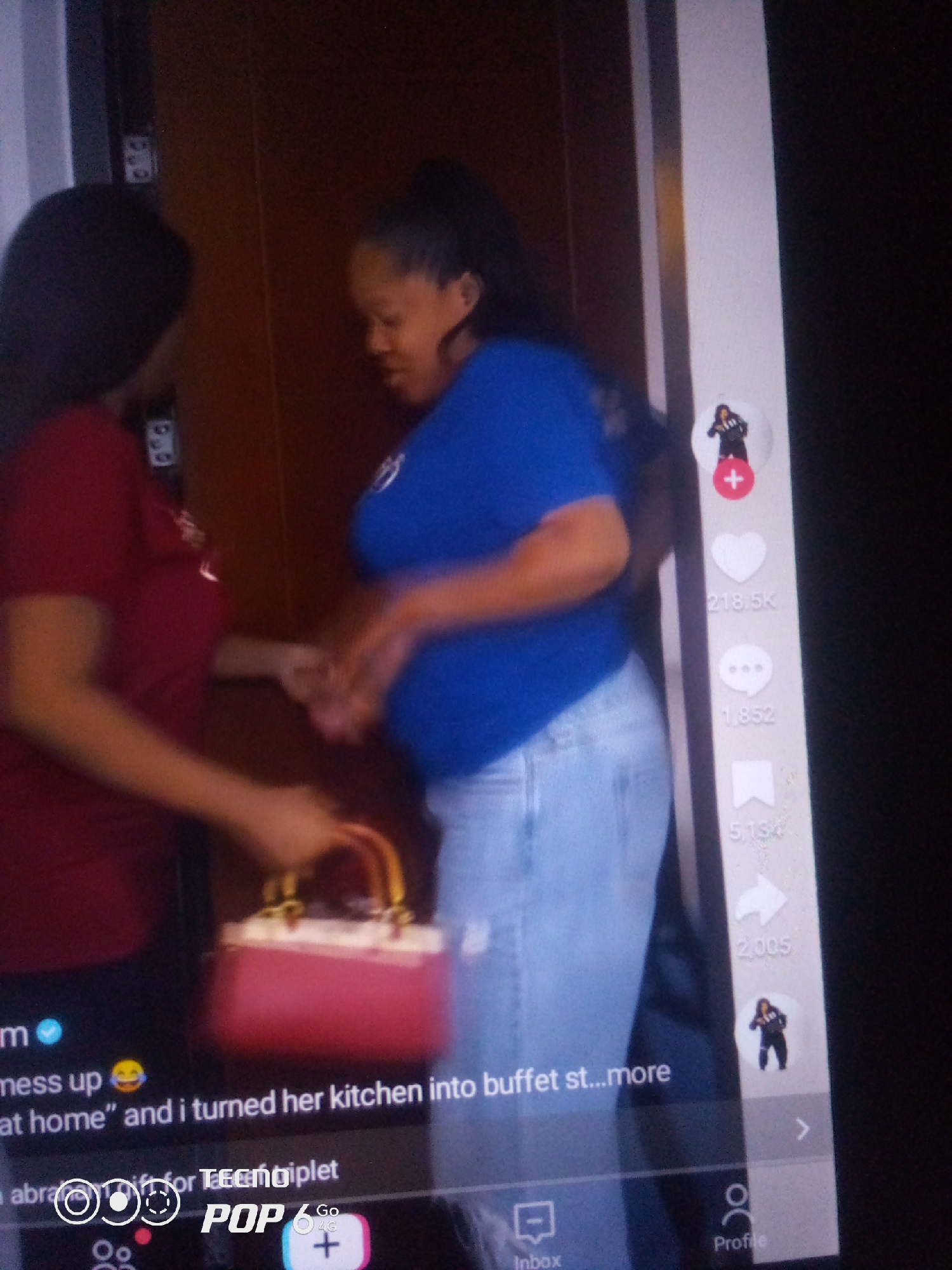 The image shows two women indoors, possibly in Nigeria, based on the text overlay "Go 4G". The woman on the left, wearing a maroon shirt, is facing away from the camera, holding a red handbag with gold accents. The woman on the right, wearing a blue shirt and light-colored jeans, is facing to the side, her body blurred by motion. She appears to be speaking or reacting to something. A digital interface overlaying the scene suggests this is a video or social media post, with elements like a heart icon with "218.5K" likes, a speech bubble icon with "1,852" comments, and an arrow icon with "5,134" shares. There is also a profile icon, an inbox icon, and a "POP 6 Go" display at the bottom. The environment appears to be a hallway or doorway with a wooden textured background. The specific location within the city of Howayi, Nigeria, cannot be determined from the provided image.
