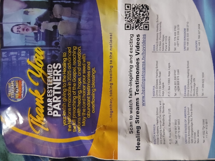 This is a crumpled, multi-colored paper leaflet with prominent blue, yellow, and white sections. The upper portion, predominantly blue and yellow, displays "Thank You DEAR ESTEEMED PARTNERS" in large script and block letters, acknowledging "lavish giving to the Healing to the Nations mandate in 2025" and offering blessings. A circular logo for "HEALING STREAMS LIVE HEALING SERVICE with Pastor Chris" is visible at the top. Embedded in this section is an image of a large screen displaying a woman with dark hair, eyes closed, and her right hand raised, appearing to be singing or praying. Below the screen, several individuals are visible from behind, dressed in suits or light-colored attire, standing and observing the screen.

The lower white section instructs to "Scan to watch faith-inspiring and exciting Healing Streams Testimonies Videos" and lists the website "www.healingstreams.tv/hovideos" alongside a black and white QR code. Below this, contact information for "Christ Embassy Healing School" is provided for multiple global regions. For Nigeria, the specified location is **21/23 Ize Iyamu Road, Ikeja, Lagos**, with an associated P.O. Box and telephone numbers; no information for Mgbidi, Nigeria is present. Other listed locations include South Africa, the United States of America, Canada, Asia, the United Kingdom, and Europe, each with specific addresses and contact numbers. The leaflet has multiple creases and minor surface imperfections, indicating handling, and rests on a dark, textured surface.
