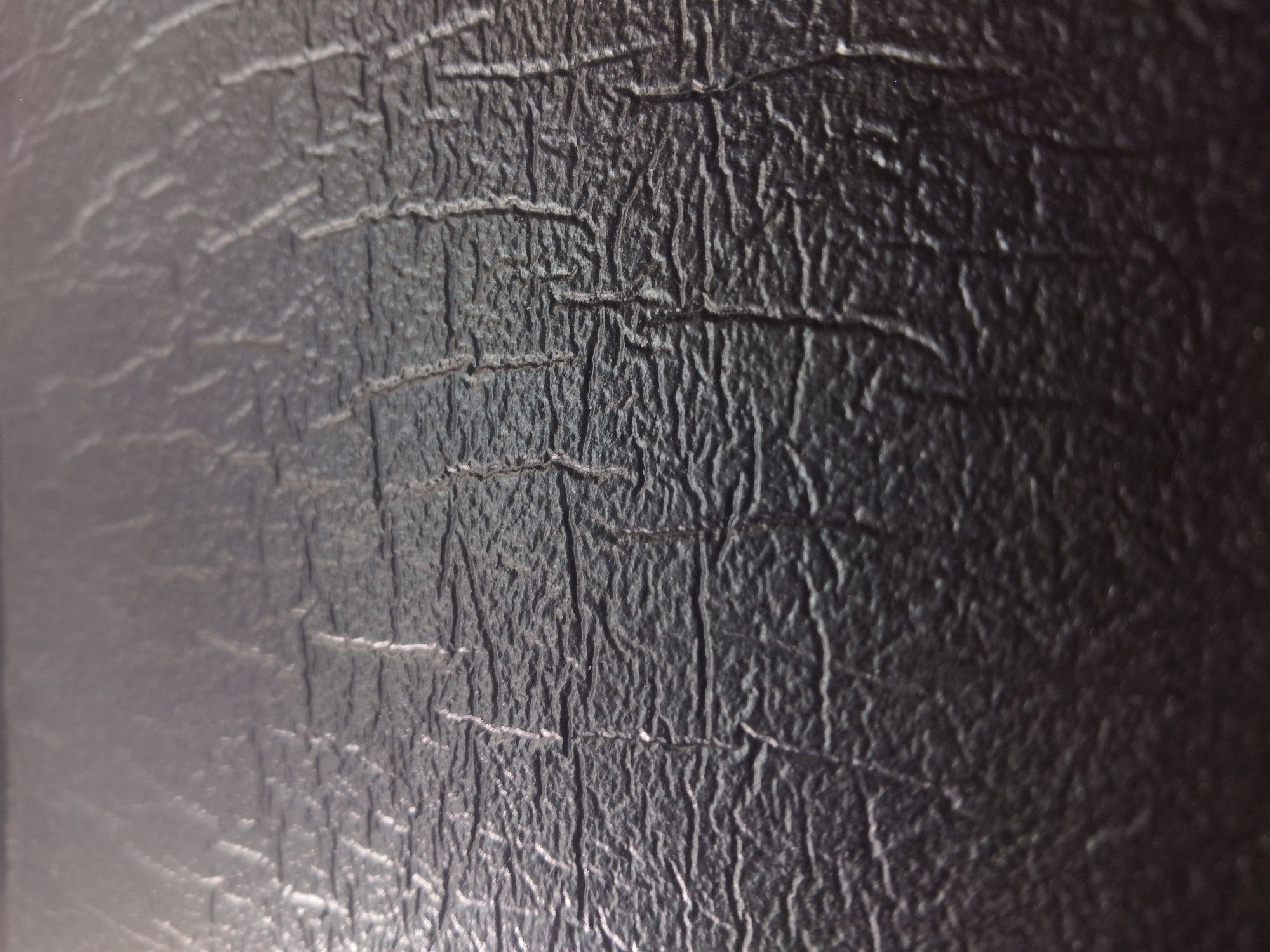 The image is a close-up, high-angle shot of a textured, dark gray surface, possibly leather or a synthetic material, with prominent, irregular horizontal and vertical creases. The lighting creates highlights and shadows, emphasizing the depth and texture of the material. There are no people, animals, or recognizable objects from an urban environment. The scene appears to be an abstract close-up of a material's surface, devoid of any specific context related to Sokolohirsk, Ukraine, or any other location.