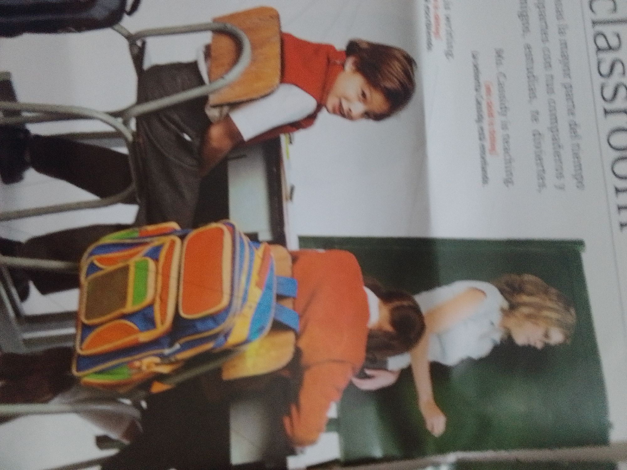 The image depicts a classroom scene in La Tagua, Venezuela. In the foreground, a child is hunched over a colorful backpack, likely engaged in packing or unpacking. Behind the child, a young person in a red shirt and white undershirt is seated on a chair, looking downwards. To the right, a woman with blonde hair, identified by the text as "Ms. Cassidy," is also seated and appears to be teaching. The scene is indoors, with the background showing what appears to be a whiteboard or projection screen with text visible. The text on the right side of the image, partially obscured, includes "classroom" and "Ms. Cassidy is teaching," suggesting an educational setting. The overall impression is one of a typical school day.