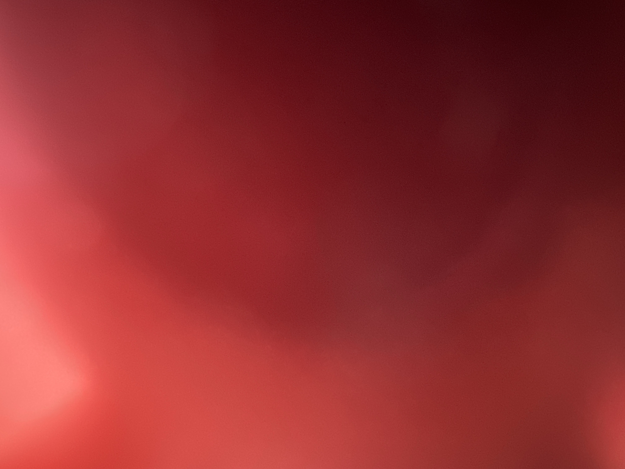 This media file is an abstract image, appearing to be a photograph with an out-of-focus lens effect or a digitally rendered abstract background. The primary colors are shades of red, ranging from bright, soft pinkish-red on the left to a deep, muted burgundy on the right. There are no discernible subjects such as people or objects. The image does not depict a specific scene or setting, nor is there any activity or event taking place. No notable details regarding time of day, weather, location cues, or emotions are present due to the abstract nature of the image. There is no visible text. The colors suggest a warm or intense atmosphere, but this is purely speculative given the lack of any representational elements.