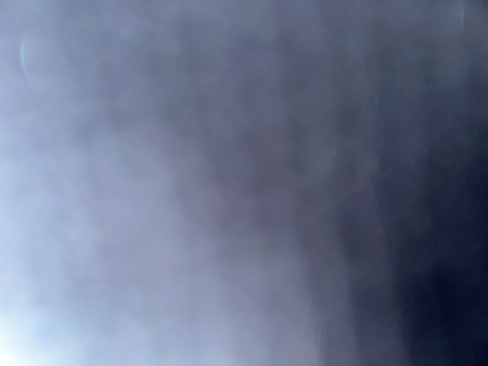 The image is a close-up, abstract shot of a gradient of colors, ranging from a bright, hazy white in the upper left corner to a deep, dark navy blue at the bottom. The texture appears soft and diffused, with no discernible objects or subjects. There are subtle hints of light flares or reflections, particularly in the upper right quadrant, exhibiting a faint rainbow hue. The overall impression is one of a smooth, atmospheric transition of light and shadow. No specific location within Bogorodskoe, Russia, can be identified from this image due to its abstract nature.