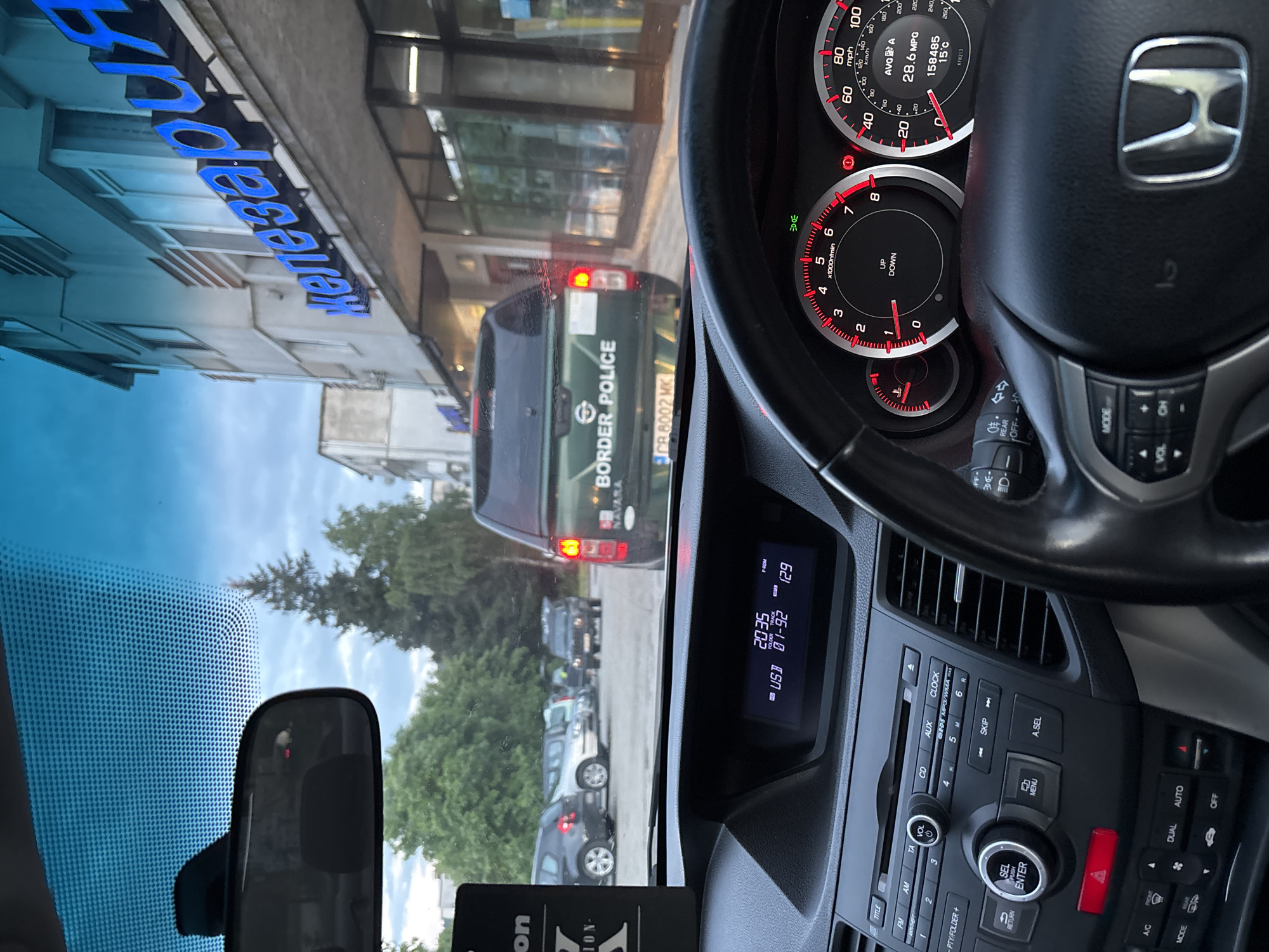 The image, taken from the interior of a car (a Honda based on the steering wheel logo and dashboard), shows a Border Police vehicle of Bulgaria directly in front. The border police vehicle has a plate number "CR 8002 MK." The car's dashboard clock displays 20:35. The car's odometer reads 158485 km, and the outside temperature is 15 degrees Celsius. Through the windshield, the reflection of a blue sign "Келешев" can be seen above a building. The GPS location is consistent with the city of Zlatograd, Bulgaria. Other vehicles are visible in the background.