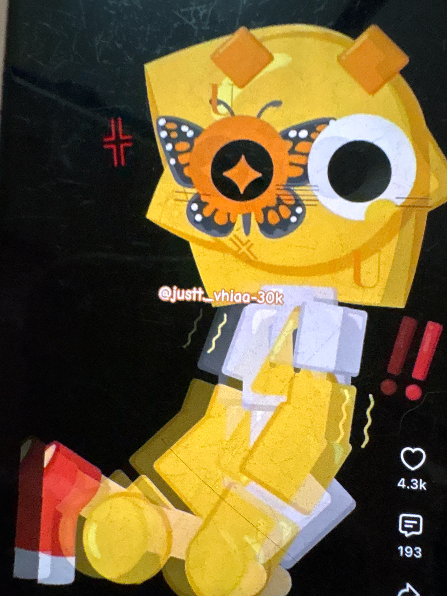 The image is a digital artwork of a yellow, anthropomorphic character with square-shaped ears and a large, round eye. The character has a butterfly design on its face. The artwork has a pixelated aesthetic and appears to be a screenshot from a social media platform, as indicated by the presence of a username "@justt_vhiaa-30k" and social media engagement metrics like "4.3k" likes and "193" comments. The background is black. There is no information in the image that suggests a location in Ashvem, India.