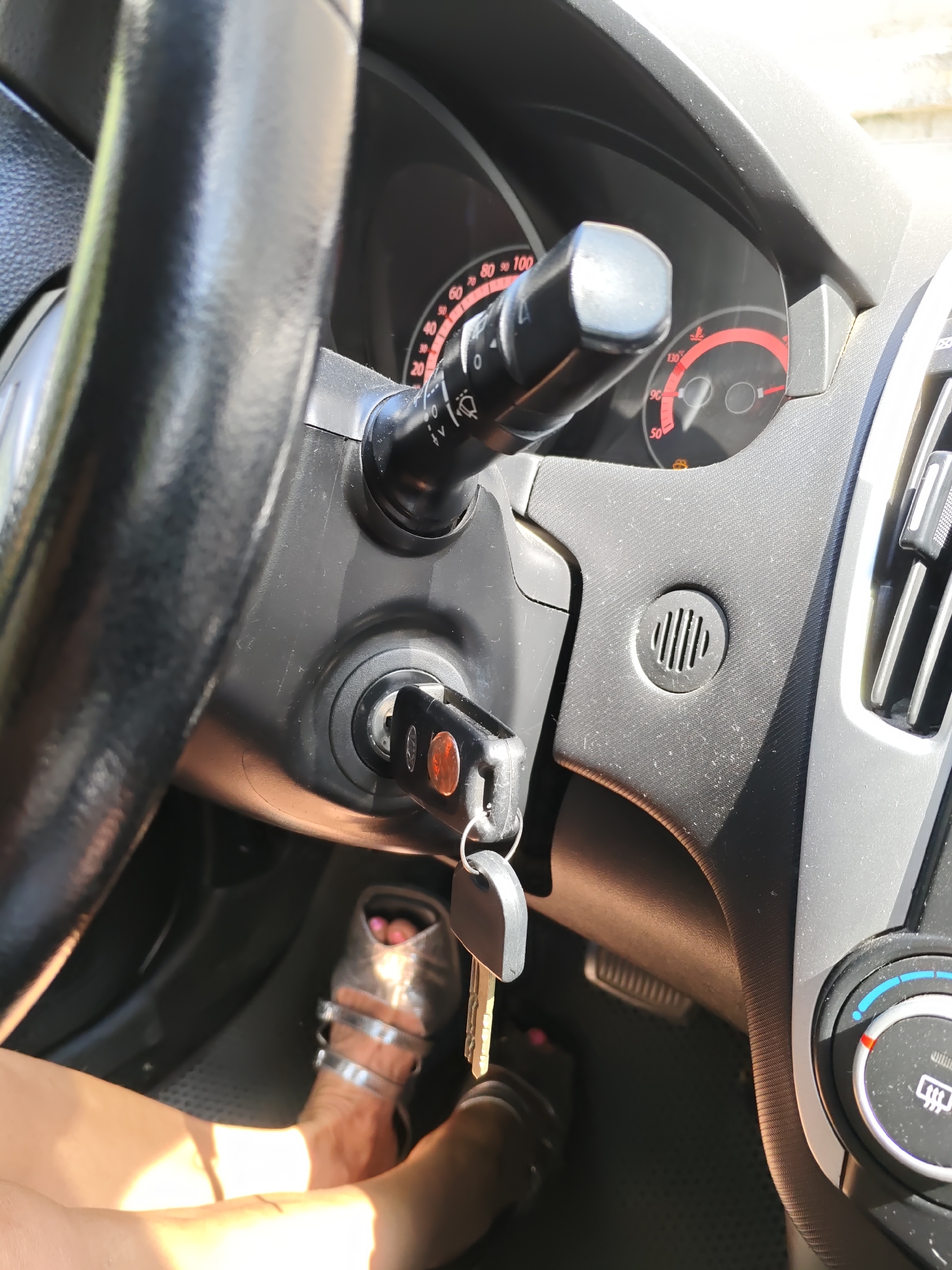 The image shows a close-up interior view of a car's dashboard and steering wheel. A car key is inserted into the ignition. A person's legs and feet, wearing silver sandals, are visible in the lower part of the frame, suggesting they are either driving or about to drive the car. The dashboard displays various gauges, including what appears to be a speedometer and a temperature gauge. The overall environment is consistent with the interior of a vehicle. The scene does not provide any specific indicators to suggest it is located in Rostov-on-Don, Russia.