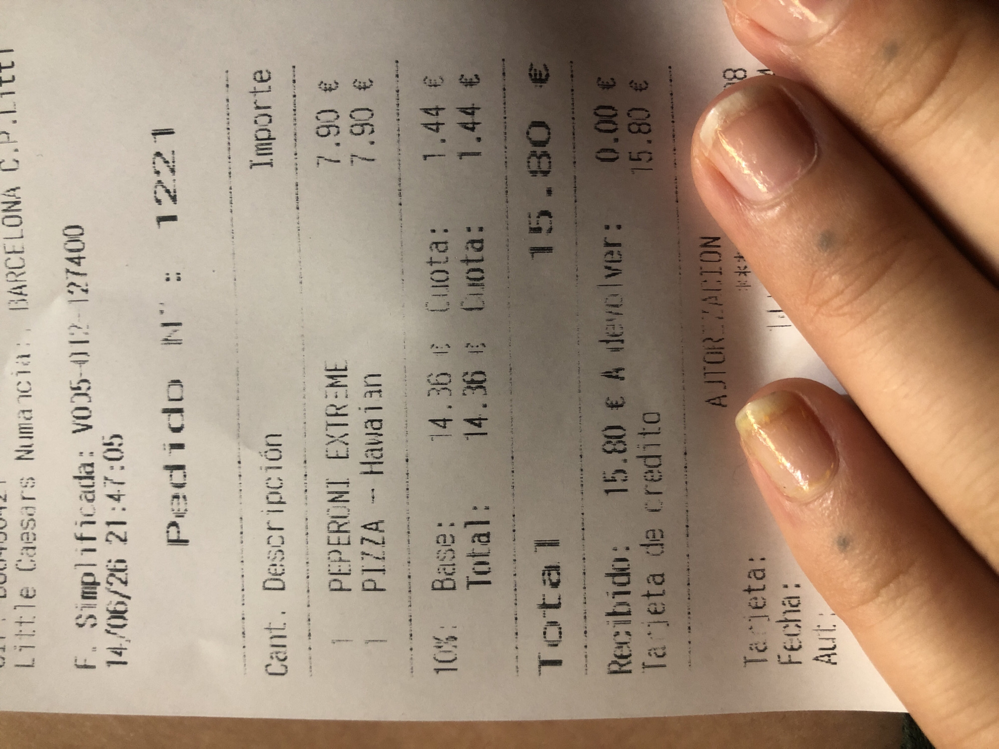 This is a close-up, top-down shot of a Little Caesars receipt, with a person's fingers in the foreground obscuring parts of the bottom of the receipt. The receipt details a food order for a "PEPERONI EXTREME" and a "PIZZA -- Hawaiian," each priced at 7.90 €. The total for these items is 15.80 €. The receipt also indicates a date of 14/06/26 and time of 21:47:05. There are details about a credit card payment, with "Recibido: 15.80 € A devolver: 0.00 €" and "Tarjeta de credito" visible. The receipt has "AJTORIZACION" printed on it. The overall environment appears to be indoors, likely at the point of sale for the restaurant. The person's fingers are well-manicured with a light polish.