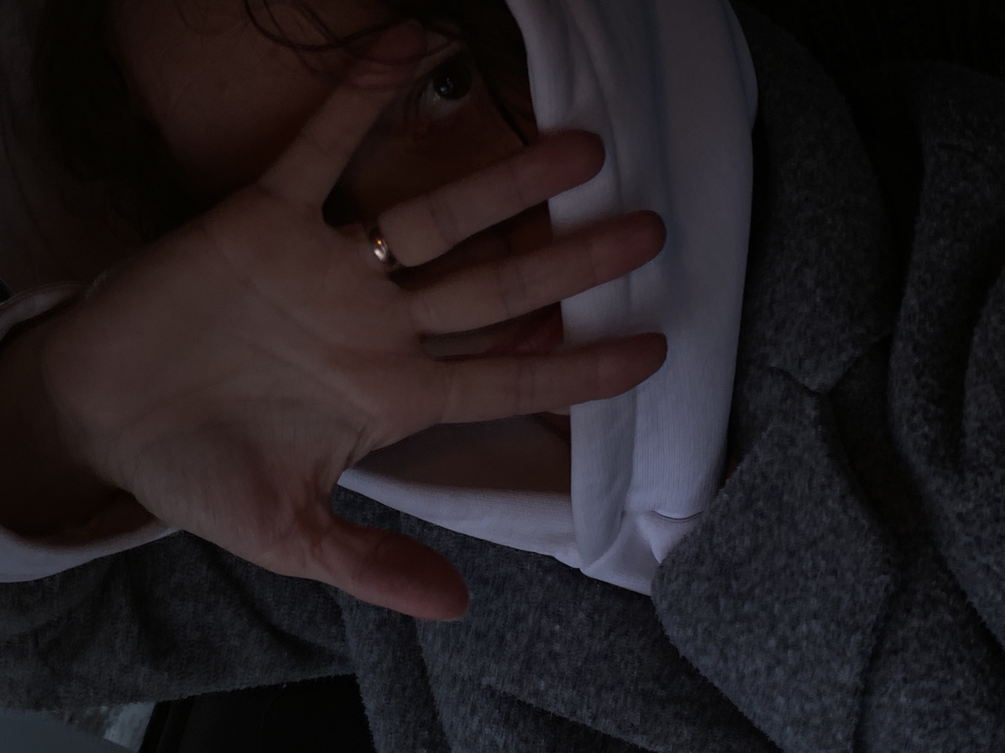 A person's face is partially obscured by their hand in an indoor setting. The individual is wearing a white hooded sweatshirt with a gray jacket or blanket covering the shoulders. A ring is visible on one of the fingers. One eye is visible. It's not possible to verify the location as Chaikovsky, Russia from the image.