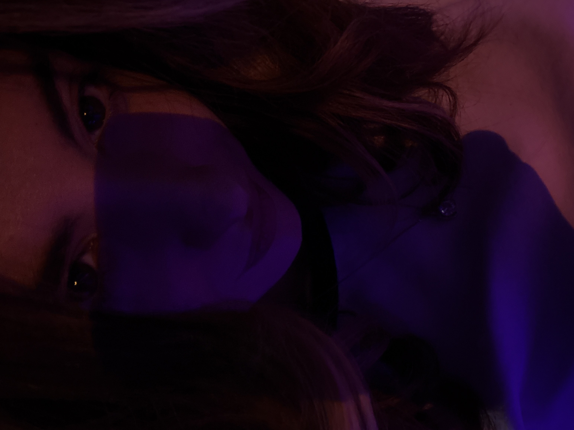 A close-up, dimly lit, angled portrait of a person. The person appears to be lying down, and their face is partially obscured by shadows and the angle of the shot. One eye is clearly visible, with dark hair framing the face. The lighting casts a purplish hue overall. A button can be seen on their clothing.
It is impossible to determine if the photo was taken in Yerevan, Armenia with the details given.