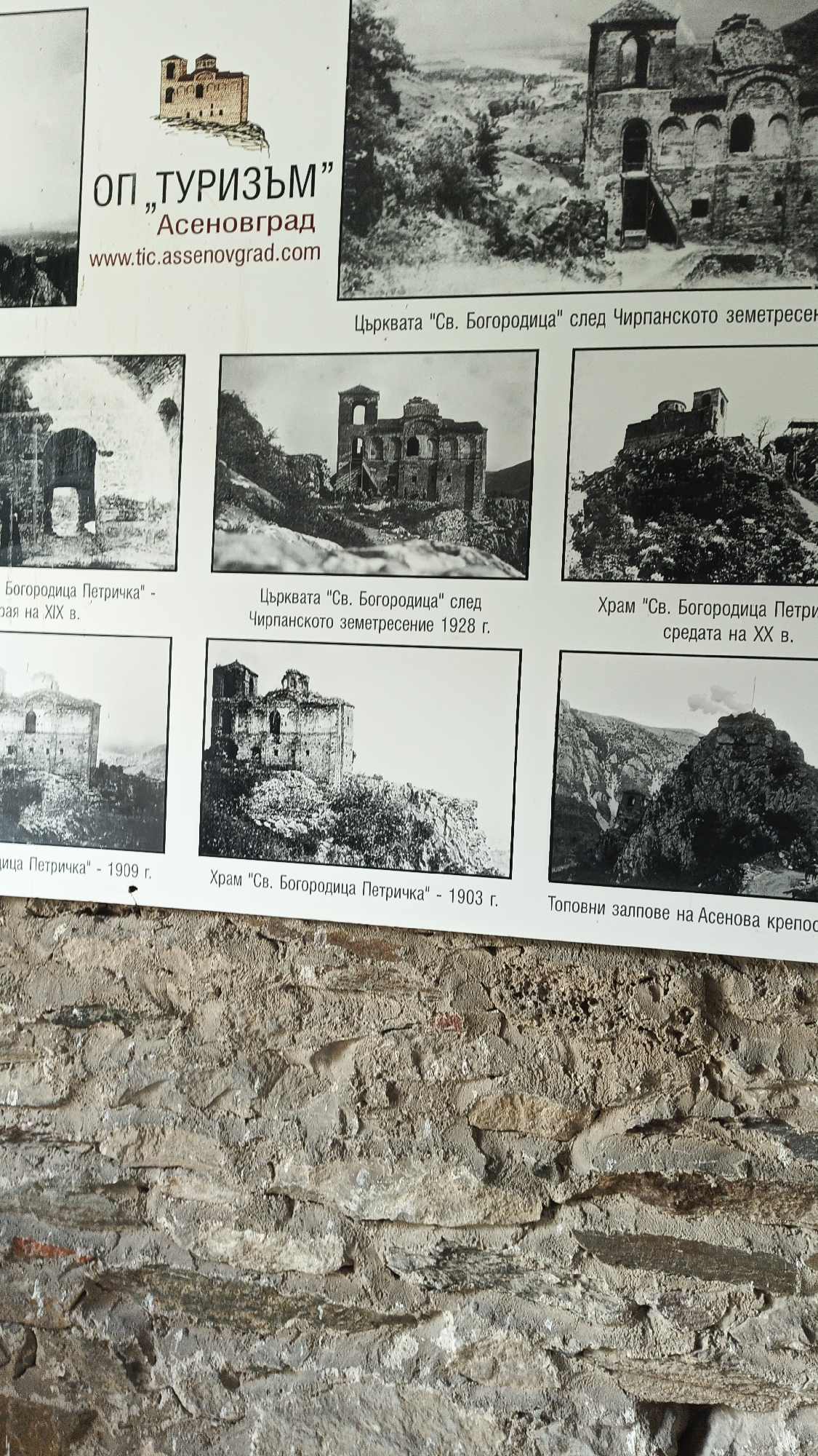 This image shows a tourism information sign affixed to a stone wall. The sign has a logo on the upper-left corner showing a cartoon-like building. The sign features six black-and-white historical images, likely old photographs. The images depict buildings in various states of ruin. Text under the images provides information in Bulgarian. The text indicates that the images pertain to churches, specifically "Св. Богородица", and mention events such as earthquakes ("Чирпанското земетресение") and dates (1903, 1909, 1928, 19th century, mid-20th century). The bottom-right image shows a mountain with stone structure. The image also includes the words "Асеновград" and website "www.tic.assenovgrad.com". The sign is attached to a stone wall.