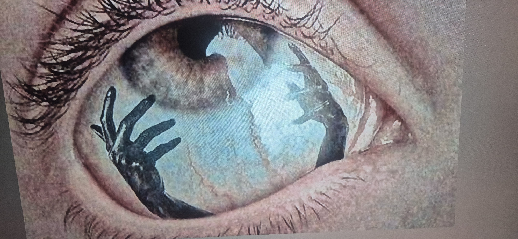 The image depicts a close-up of an eye. Reflected in the iris are two dark, skeletal hands reaching upward. The eye itself is surrounded by eyelashes and skin with visible texture. There are no identifiable details linking this image to Yerevan, Armenia.