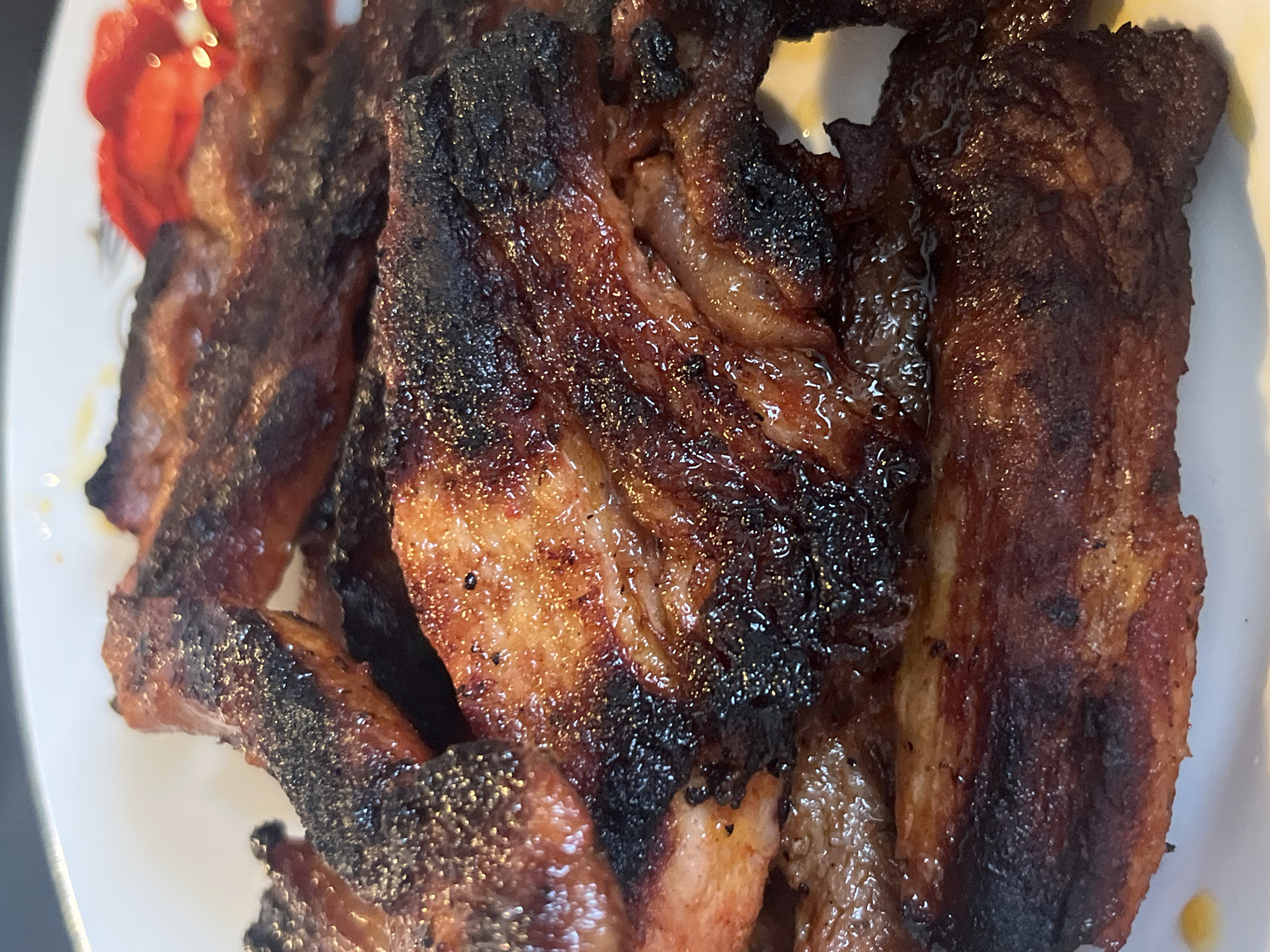 The image depicts cooked pork ribs on a white plate, possibly porcelain, adorned with a faded red floral design. The ribs exhibit a combination of golden-brown and dark charring. The location is unknown and cannot be inferred from this image.