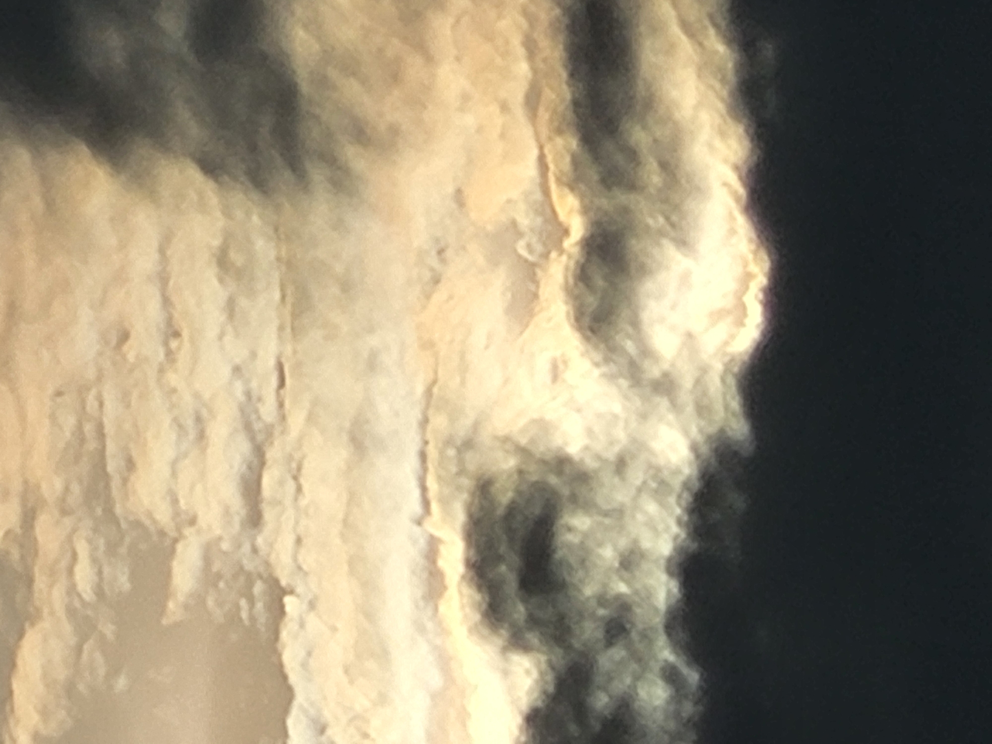 The image is a close-up, abstract view of clouds. The clouds are illuminated from behind, creating a glowing effect in some areas and casting dark shadows in others. The textures are soft and diffused, with wisps and streaks of light and dark. The overall impression is one of dramatic, ethereal light. The specific location in the city of Unknown, Unknown cannot be determined from the image.