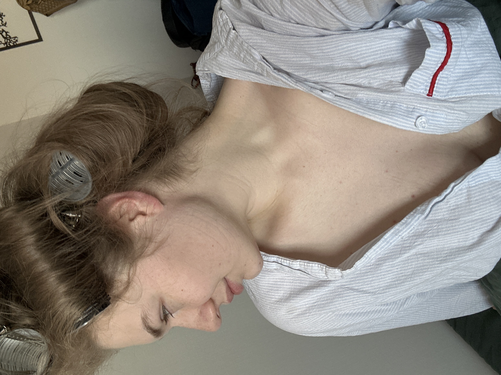 A woman is lying down, facing left. She has brown hair with rollers in it. She is wearing a light blue and white striped shirt. Her skin is pale. The location is not identifiable as Kazan, Russia from the given image.