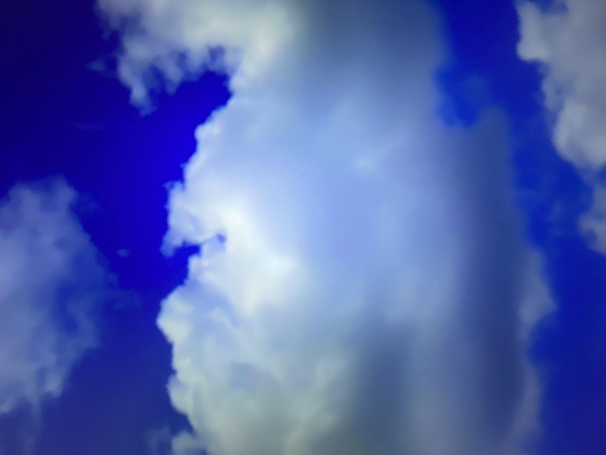 The image shows a sky with clouds. The sky is a deep blue, and there are several white and gray clouds scattered throughout. The clouds vary in size and shape, with some appearing fluffy and others more wispy. The lighting suggests it is daytime, and possibly sunny, with the sun illuminating some of the clouds from behind. There is no indication of the city of Kołobrzeg, Poland, or any specific urban environment in the image. The scene is purely natural, depicting the sky and clouds.