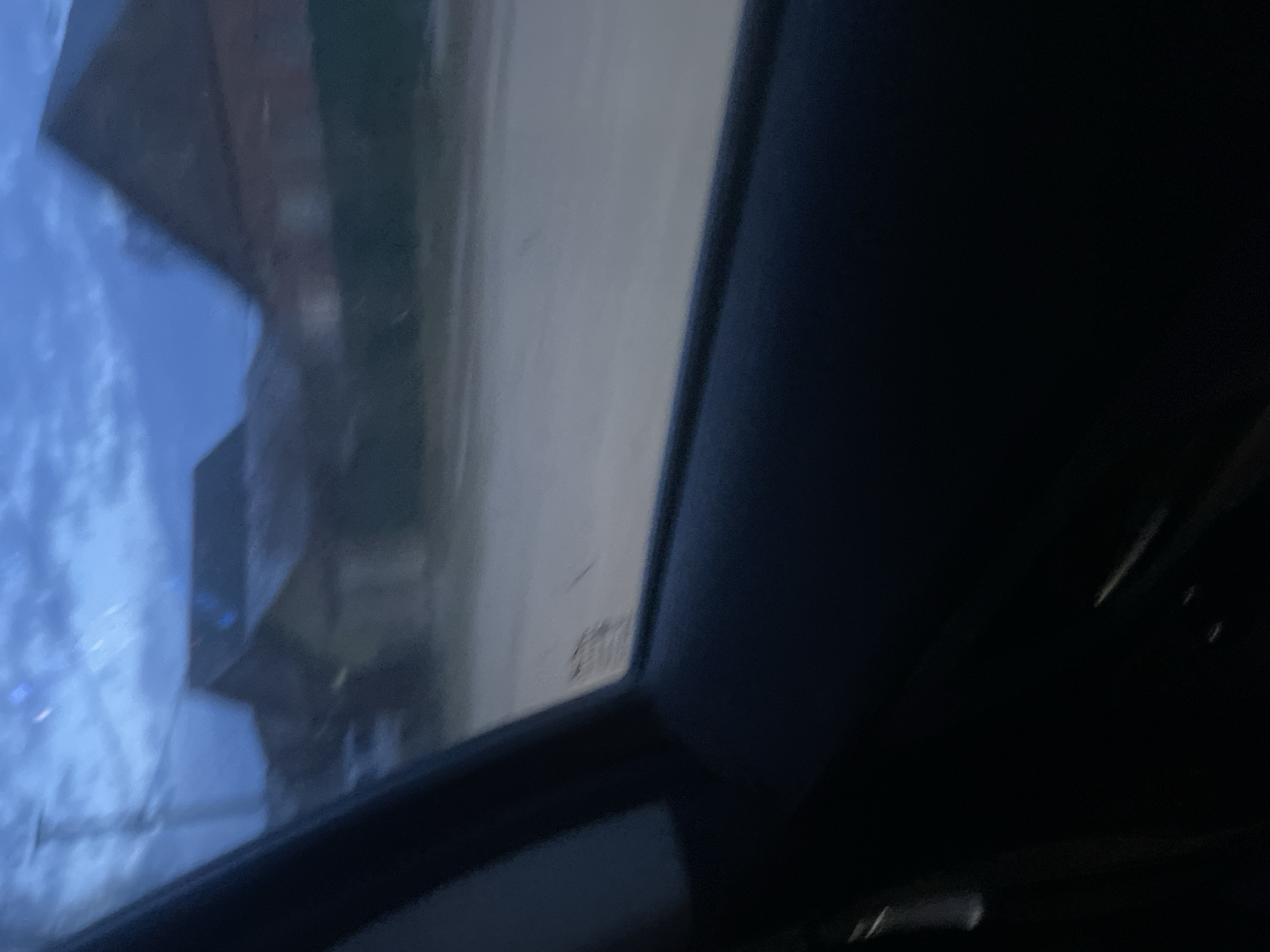 The image appears to be taken from inside a vehicle, looking out the side window. The view is partially obstructed by the car's frame. Outside the window, there is a street or road, and a building is visible, slightly distorted by the glass. The sky is visible. Due to the angle and lack of detail, precise identification of the location in Chaikovsky, Russia, is impossible.