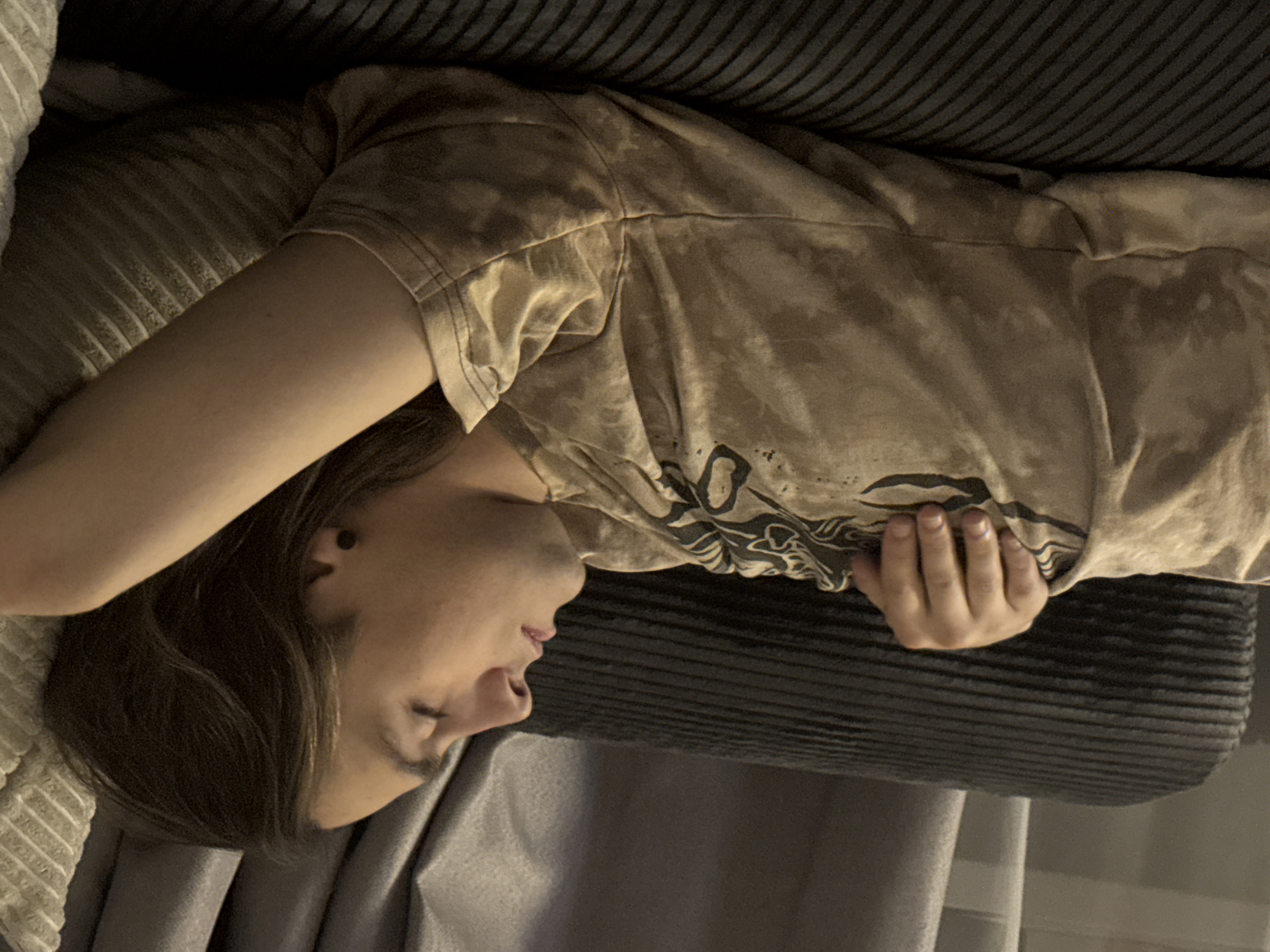 A person is lying on a sofa. The person is wearing a t-shirt. They are resting their head on a light grey cushion and have their hand resting on a dark grey cushion. The background includes a light grey curtain. The location of Khimki, Russia is not discernible from the provided image.
