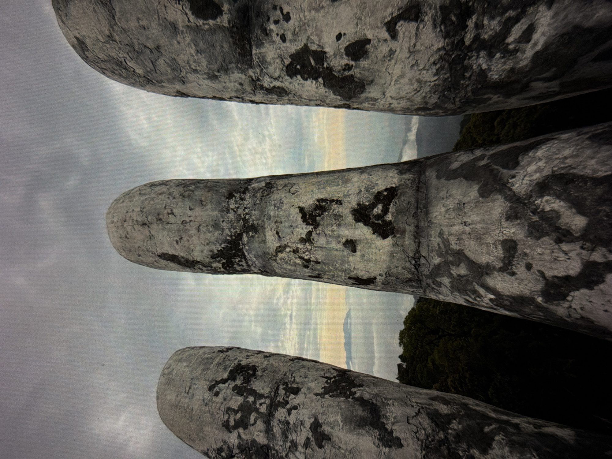 The image shows a perspective view of the Golden Bridge at Ba Na Hills in Đà Nẵng, Vietnam. Three large, stone-like hands are visible, creating the illusion of giant hands holding up the pedestrian walkway. The sky is overcast and partly visible through the gaps between the “fingers”. Trees are also visible in the background.