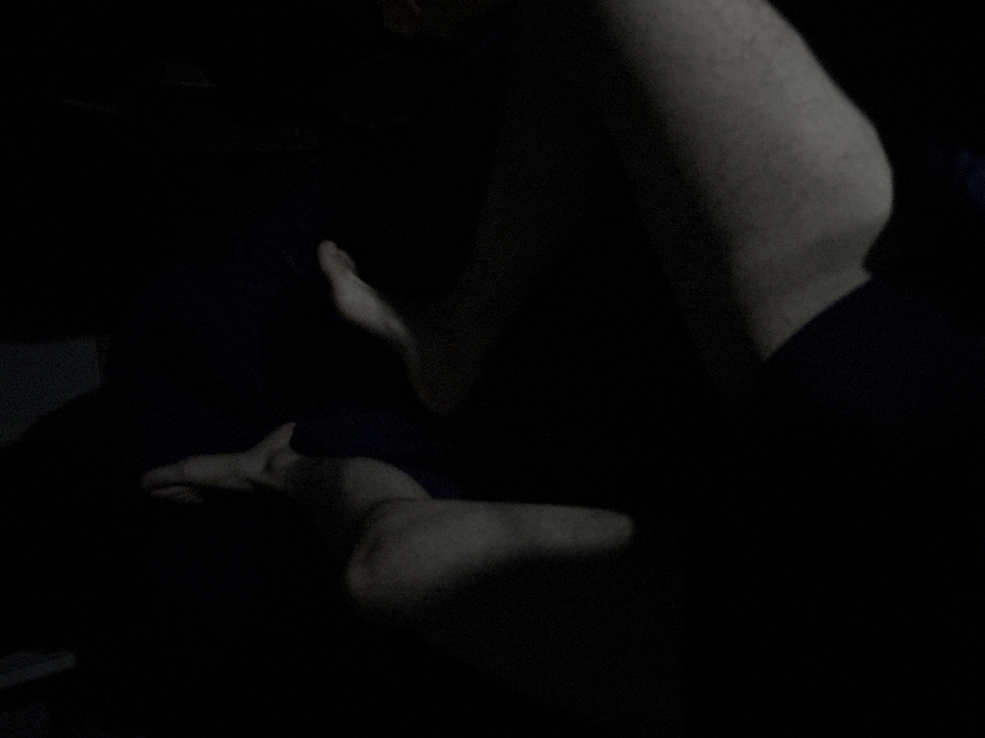The image depicts a person lying on a dark surface, possibly a bed or sofa, in a dimly lit environment. The person is partially visible, with their torso and legs illuminated by a weak light source. The lighting conditions and the angle of the photograph make it difficult to discern precise details about the individual's features or the immediate surroundings. The location is unknown; there is no information to place this photograph in Yerevan, Armenia.