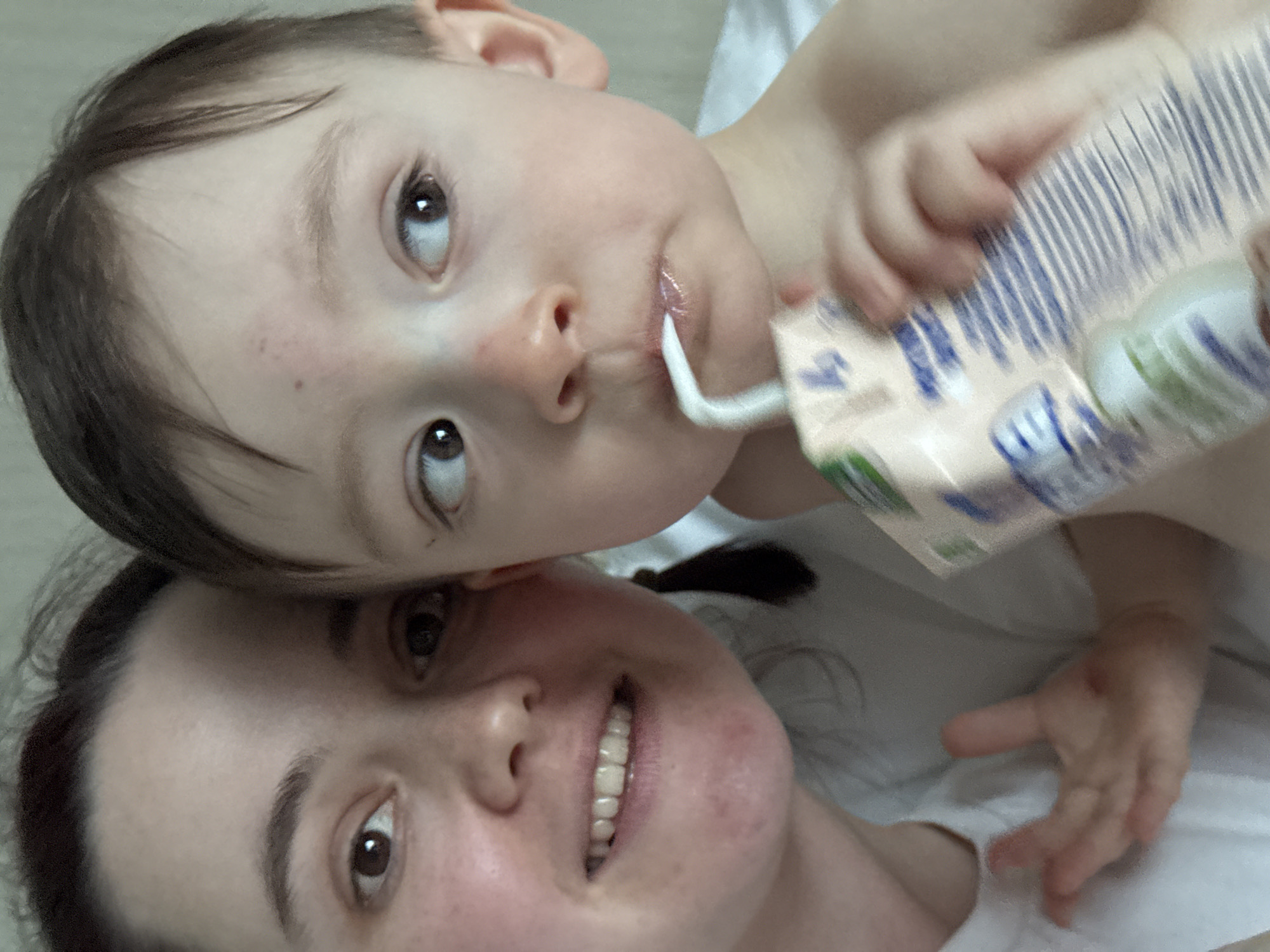 A close-up shot shows a woman and a young child. The child is holding a drink carton with a straw in his mouth. The woman is smiling. The image appears to have been taken indoors, possibly in a home setting. There is no information in the image to indicate it was taken in Sochi, Russia.