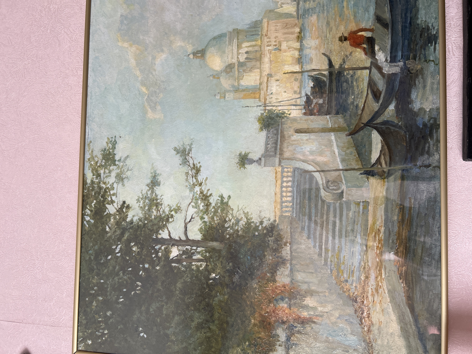 The painting depicts a canal scene in Venice, Italy. In the foreground, two gondolas are visible on the water. One gondola is empty, while the other has a person wearing a hat and an orange shirt seated in it. Further in the background, a large, domed building with classical architecture stands prominently on the other side of the canal. The water reflects the sky and the surrounding buildings. On the left side of the painting, a stone staircase leads up to a balcony lined with a balustrade. Lush green trees with dappled sunlight filter through their leaves are situated next to the staircase. The sky is cloudy, with soft blues and whites dominating the upper portion of the image. The overall atmosphere is serene and picturesque, capturing the essence of a Venetian waterway.