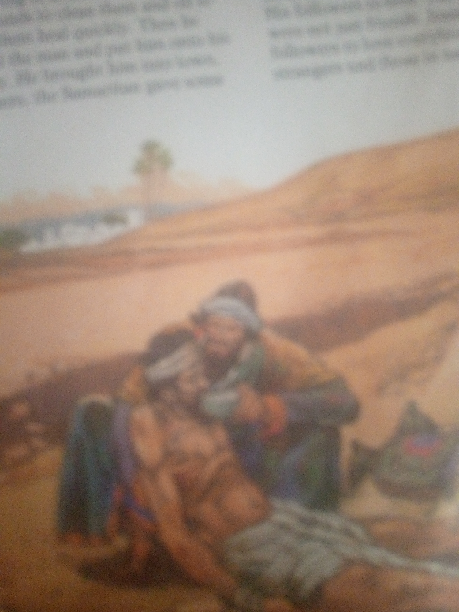 The image depicts a scene from a book, showing a painting or illustration of a man being tended to by another individual. The setting appears to be an arid, desert-like landscape with rolling hills in the background. In the foreground, one man, lying down, is being cared for by a second man who is kneeling beside him. The kneeling man, wearing a green garment and a head covering, is attending to the injured man. The injured man, whose body is partially visible, is draped in a cloth. There is also a bag or bundle placed near them. The image is blurry and lacks sharp detail, making precise identification of individuals and their clothing difficult. The text accompanying the image is also mostly illegible due to the blur. The location in the city of Jauro Yinu, Nigeria, is not depicted in this image and is therefore not described.