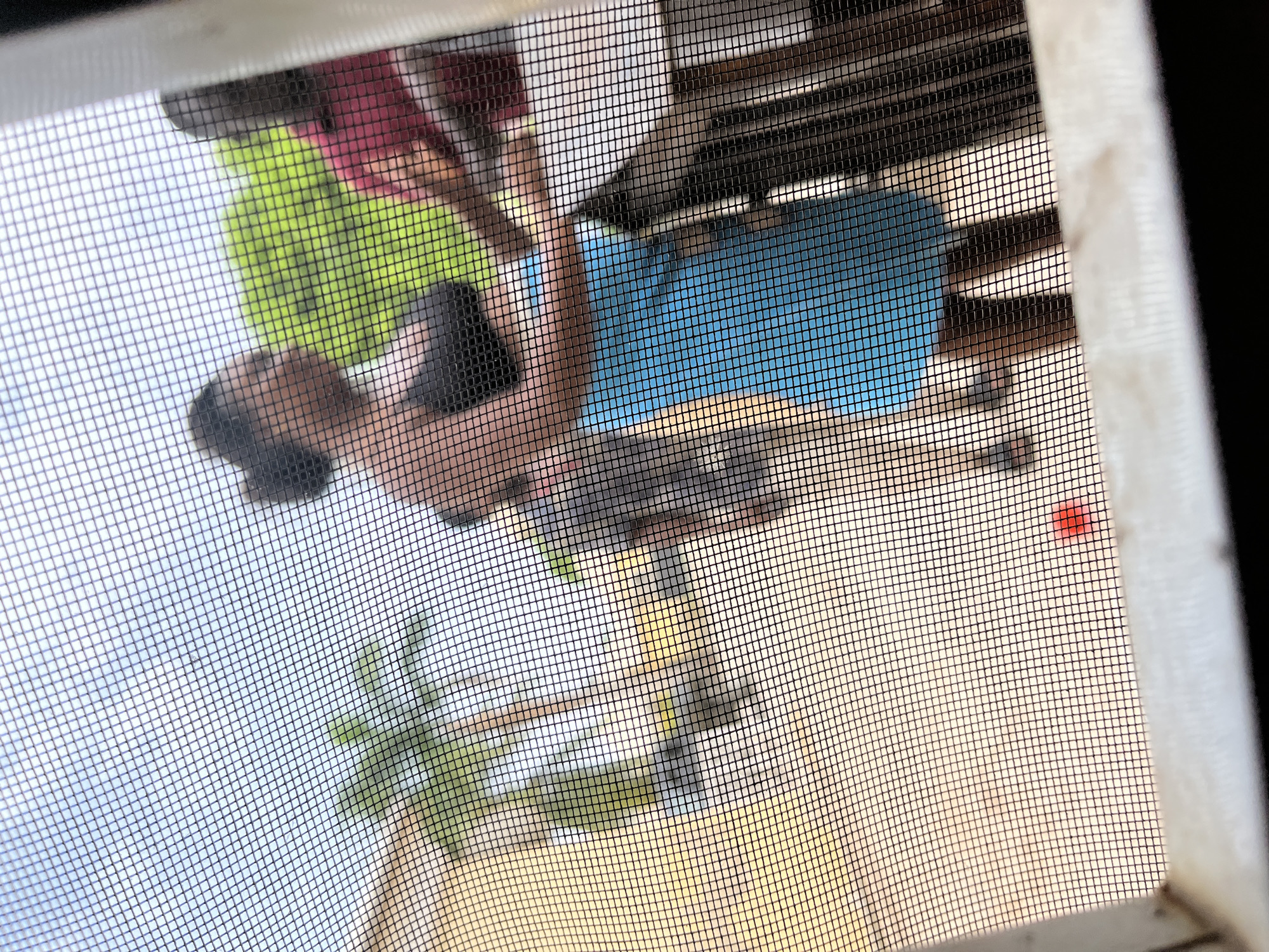 Through a window screen, a partially visible group of people stand on a balcony or veranda. One person wears a pink shirt and another a green shirt. A partially visible body of water is beneath the balcony. A palm tree is visible near the base of the image, in the lower left quadrant. The location is likely Abuja, Nigeria based on the prompt.