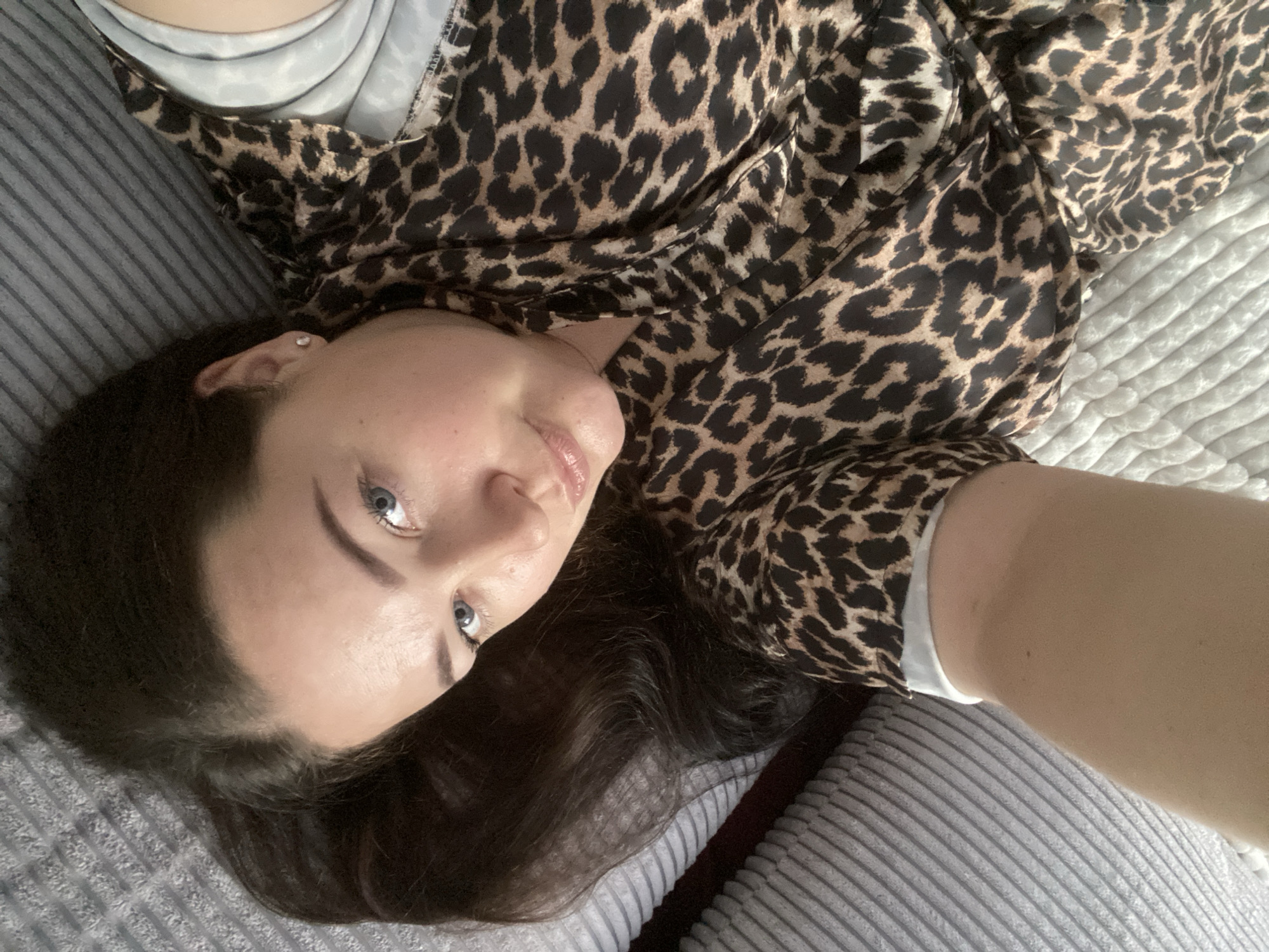 A woman with blue eyes and dark hair is lying on a grey, ribbed surface. She is wearing a leopard-print top over a white shirt. She appears to be taking a selfie. There is no indication of the city of Sochi, Russia.