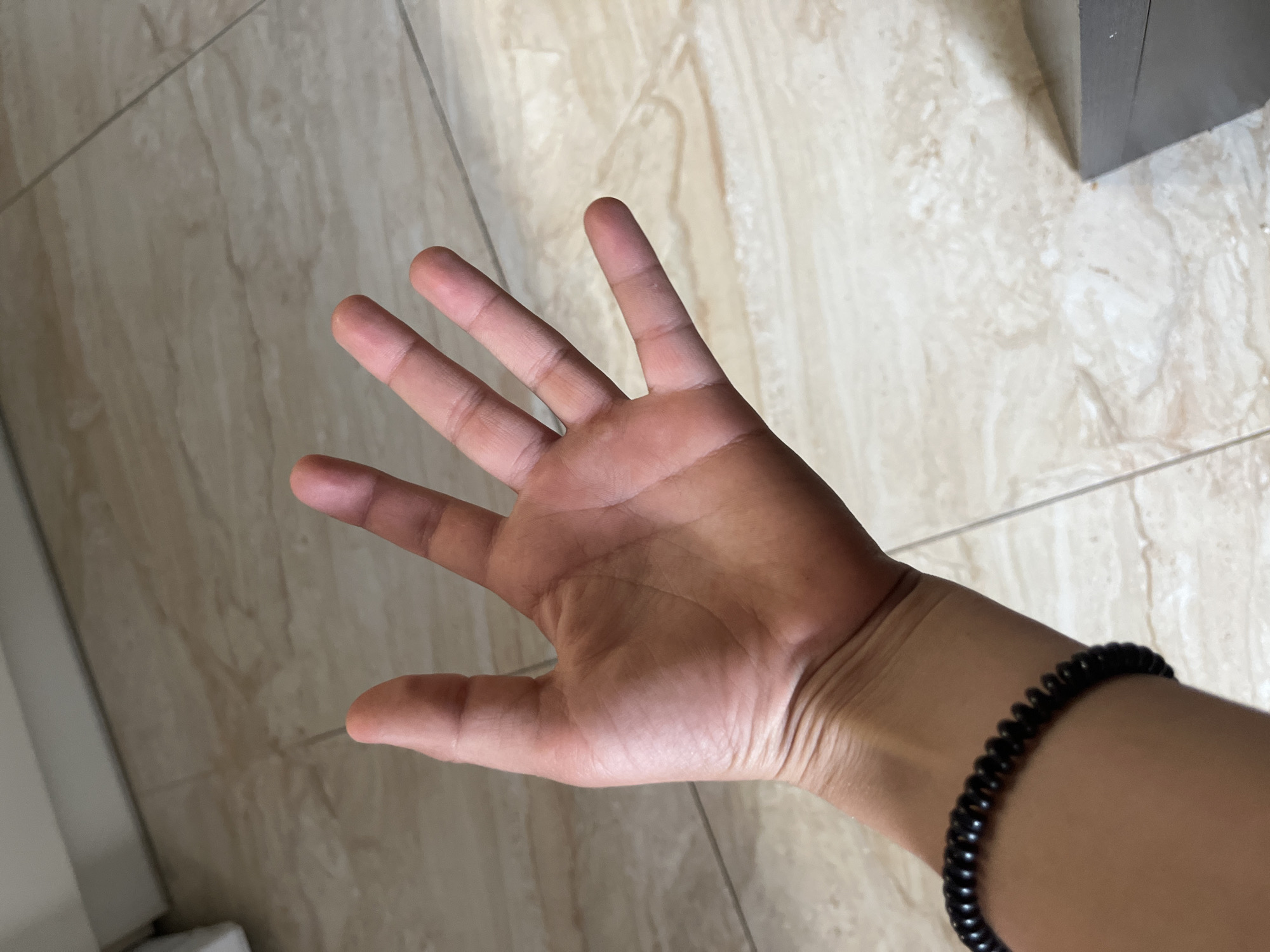 The image shows an open right hand with fingers extended against a background of beige tile. A black beaded bracelet is visible on the wrist. The location of the image is not discernible as Chaikovsky, Russia.