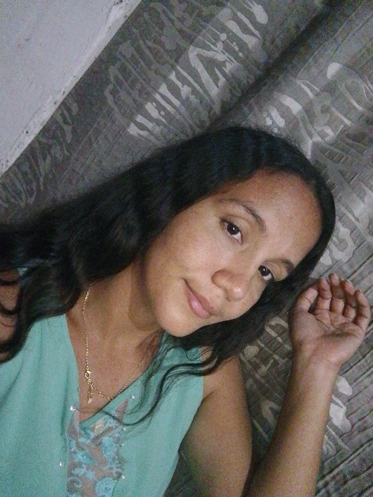 A medium shot captures a person with dark hair, wearing a light blue top and a gold necklace, lying on a surface covered with a grey and white patterned material. The location of Juan Griego, Venezuela, is not discernible from the image.