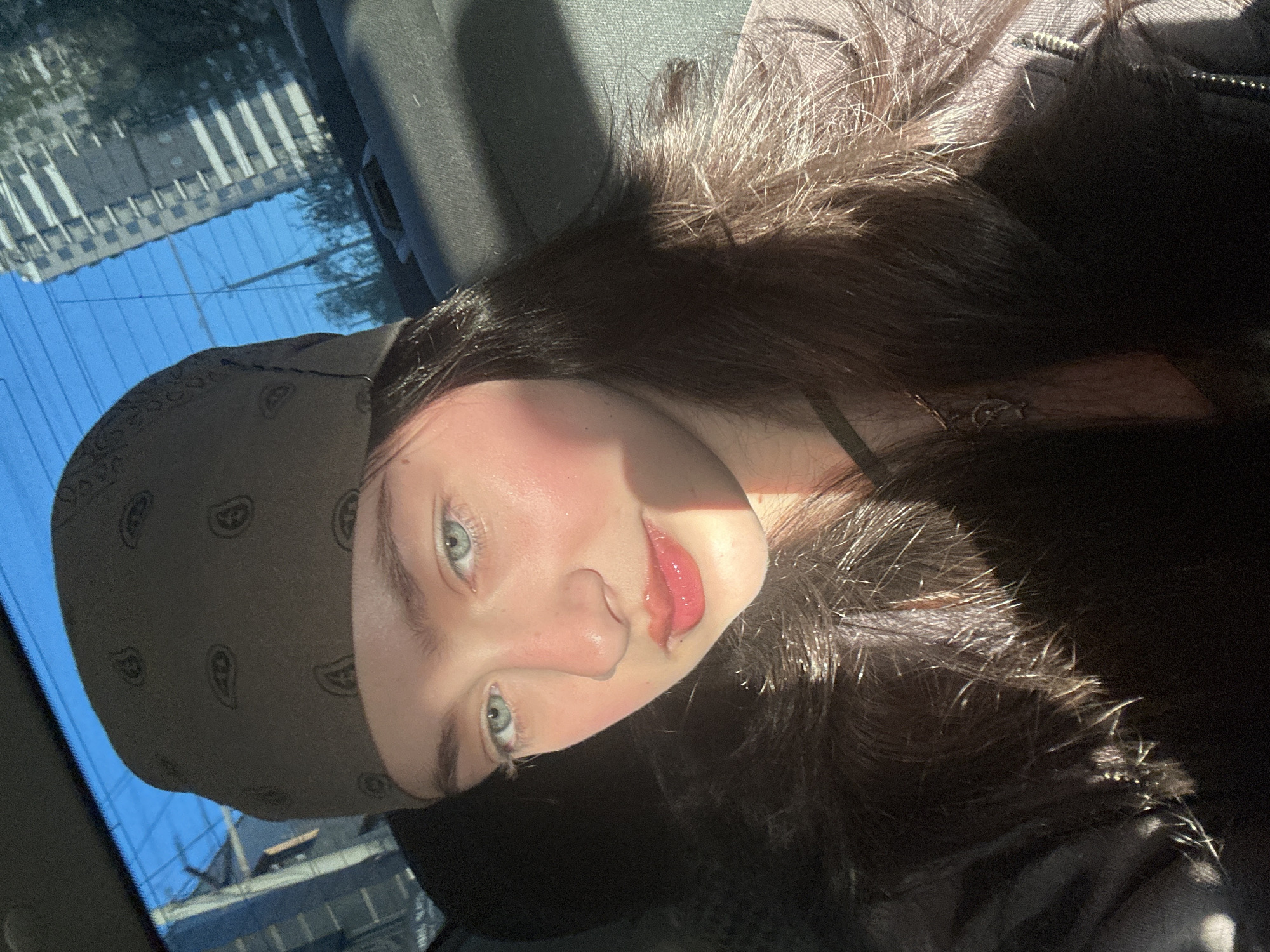 A person is in the passenger seat of a car. The person is wearing a paisley print bandana. The reflection of a tall building and a blue sky are seen through the window. No information can be determined about the city of Yerevan, Armenia.