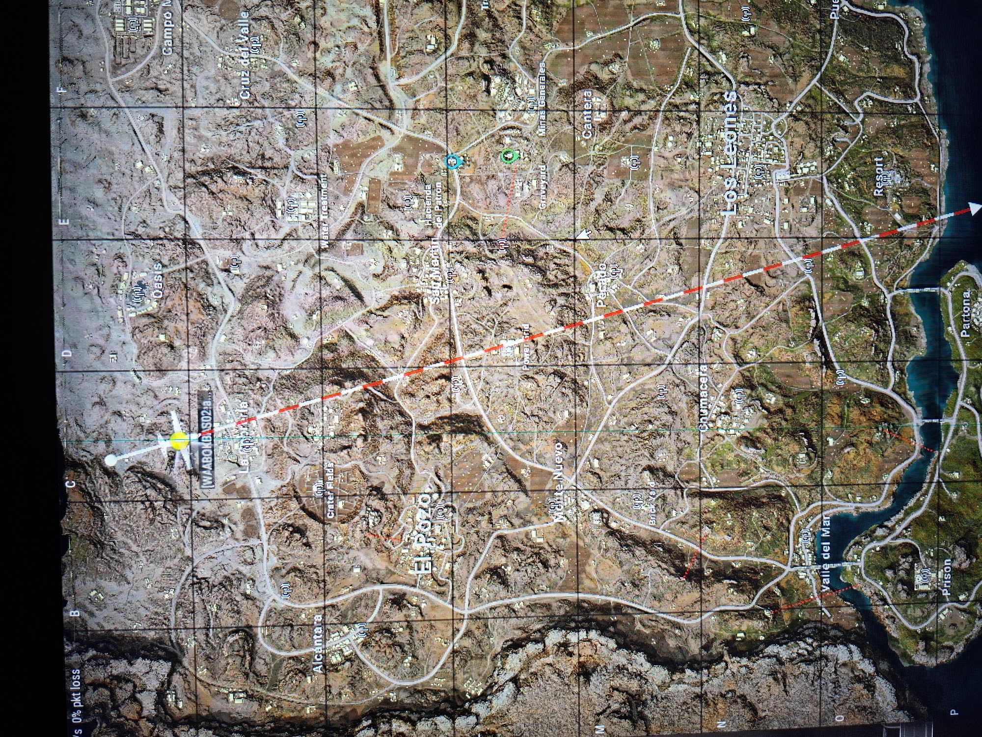 The image shows a map of a location from a video game. The map is divided into a grid with labeled rows and columns (A-P, 1-16). The map features a variety of terrains, including mountains, deserts, and coastal areas. There are several towns and settlements marked on the map, such as "El Pozo", "Los Leones", and "Oasis". A red dotted line marks a trajectory across the map, from "WAABOKBAS02" near the top-left to the "Resort" near the bottom right. A yellow compass icon is positioned above the "WAABOKBAS02" marking. There are also other objects of interest on the map, such as roads, rivers, and landmarks. The map appears to be a strategic tool within the video game, used for navigation and planning.