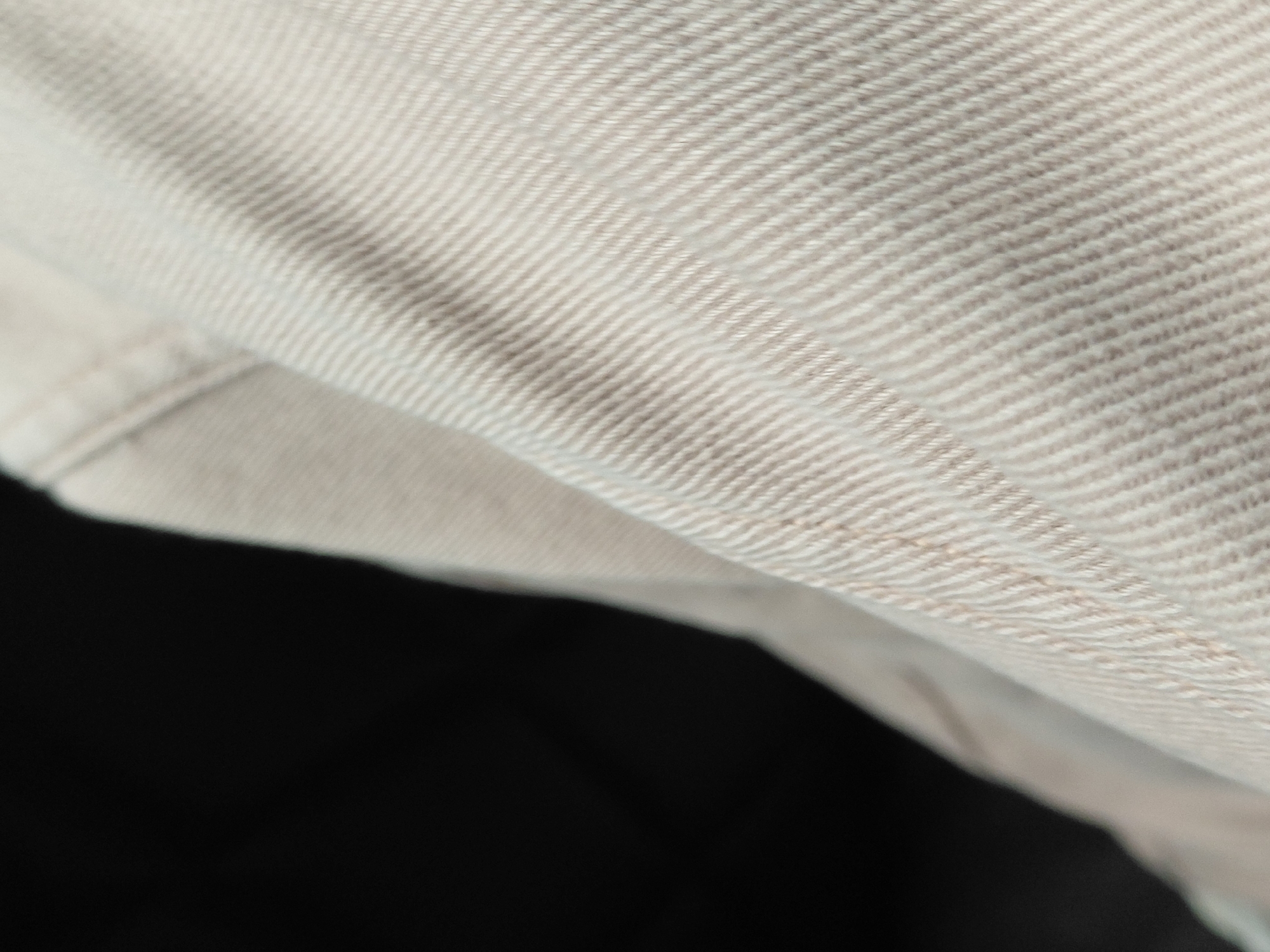 The image shows a close-up of a beige fabric with a textured weave and a visible seam. The fabric is folded over, with a portion of the image occupied by a dark, indistinct area. There is no information to suggest a specific location in Santa Ana, Venezuela, or any people, subjects, objects, actions, interactions, or environmental details beyond the described fabric.