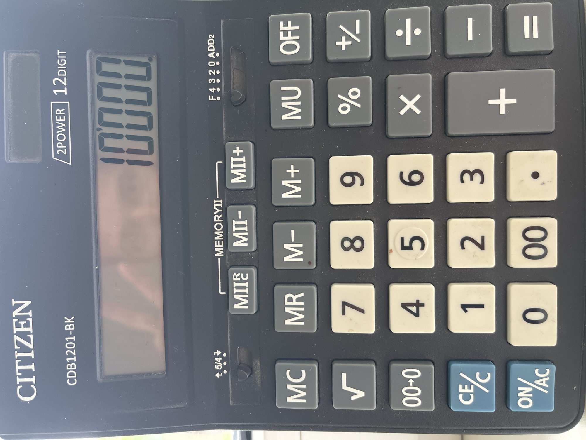 A Citizen CDB1201-BK calculator displays "10000" on its 12-digit screen. The calculator features a black and grey color scheme, with function keys arranged above the number pad. The scene is indoors. There are no people in the scene. The location in the city of Chaikovsky, Russia is not apparent.