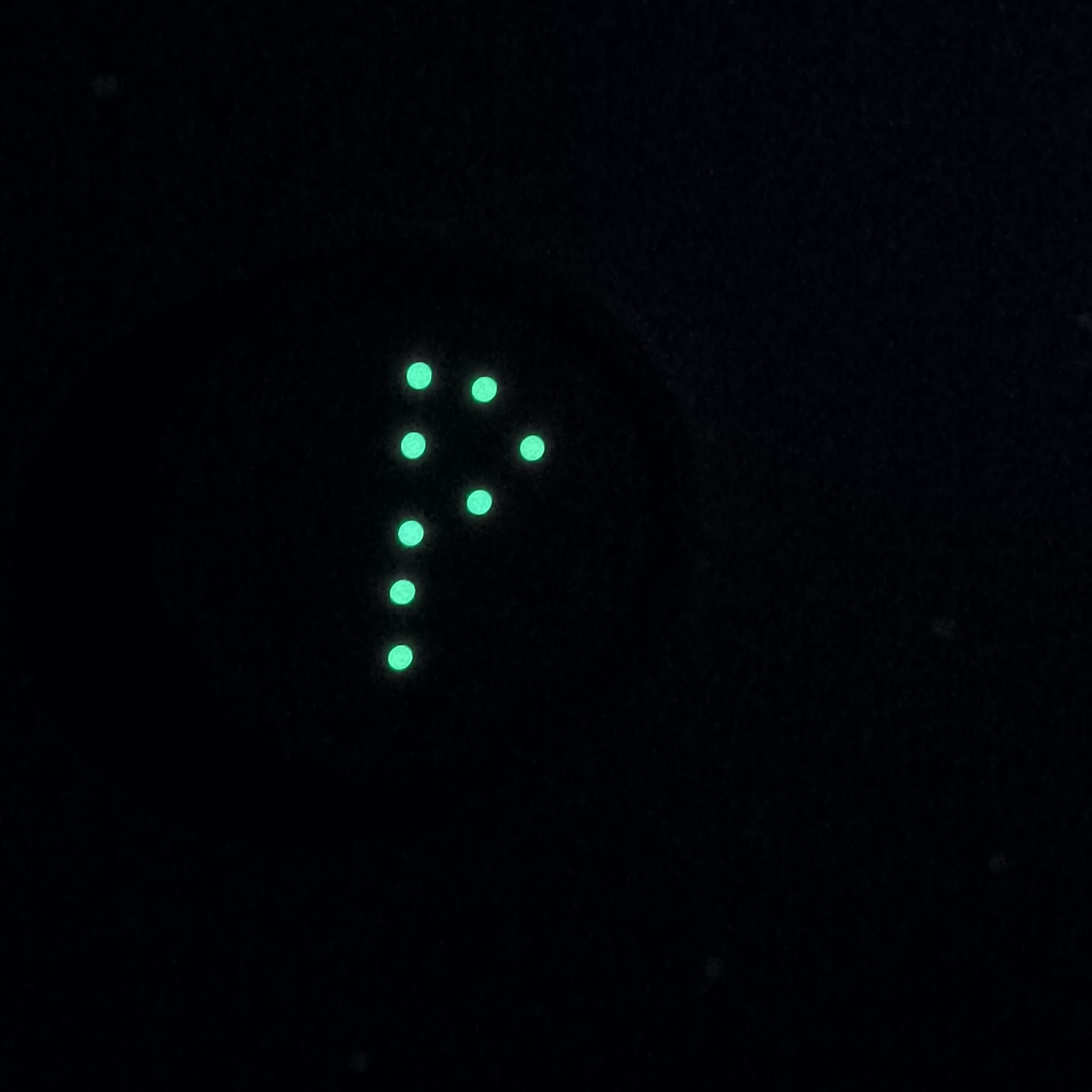 The image displays a dark background with several small, glowing green dots arranged in a shape that resembles the letter "P". The dots are circular and appear to be self-illuminating or illuminated from behind. The arrangement suggests a patterned display or a representation of something abstract. There are no discernible people, objects, or environmental features that can be identified as belonging to the city of Varna, Bulgaria. The scene is minimalist, focusing solely on the luminous dots against the dark backdrop.