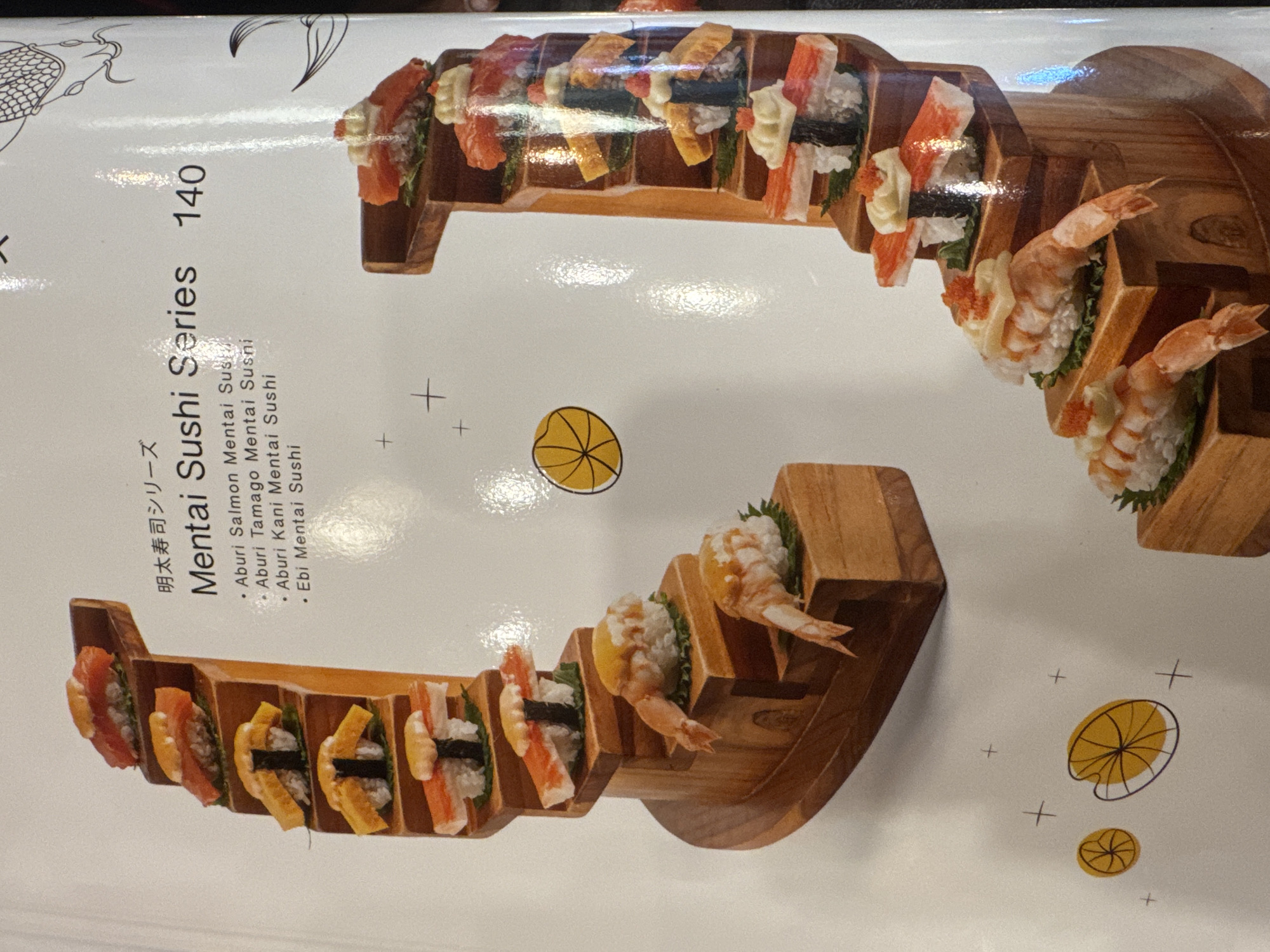 This is an eye-level photograph of a menu showing a style of sushi. The sushi is arranged in ascending, stepped, wooden containers. The sushi on the top consists of salmon, tuna, eggs, and kani. The sushi on the bottom consists of Kani and Ebi. The text reads, "Mentai Sushi Series 140" and "Aburi Salmon Mentai Sushi" followed by the varieties of sushi. It is not possible to locate this photograph in Kuta, Indonesia.