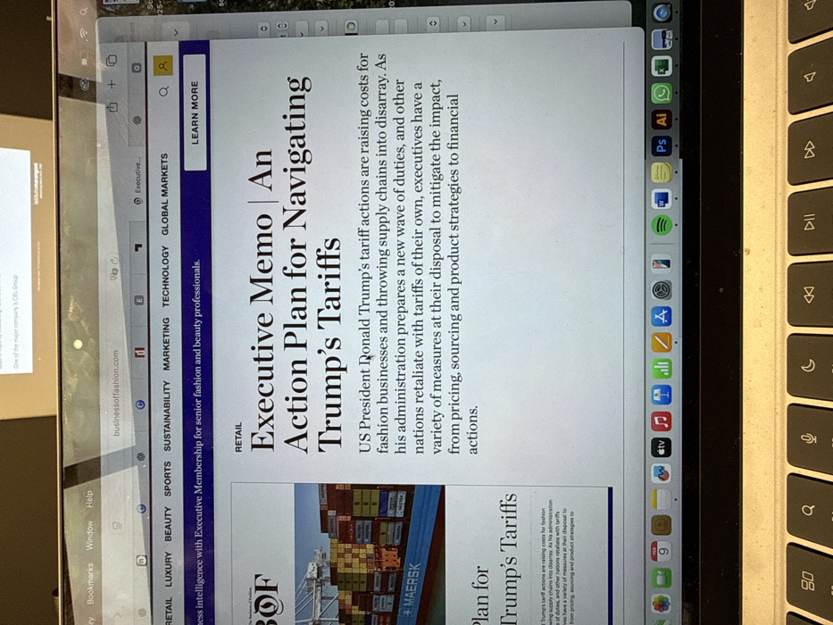 The image shows a laptop screen displaying an article from the website "businessoffashion.com." The article, titled "Executive Memo | An Action Plan for Navigating Trump's Tariffs," discusses the impact of US President Donald Trump's tariff actions on the fashion industry. The article highlights the rising costs for fashion businesses, the disruption of supply chains, and the strategies executives can use to mitigate the financial impact. There's also an image of shipping containers with the logo "MAERSK."