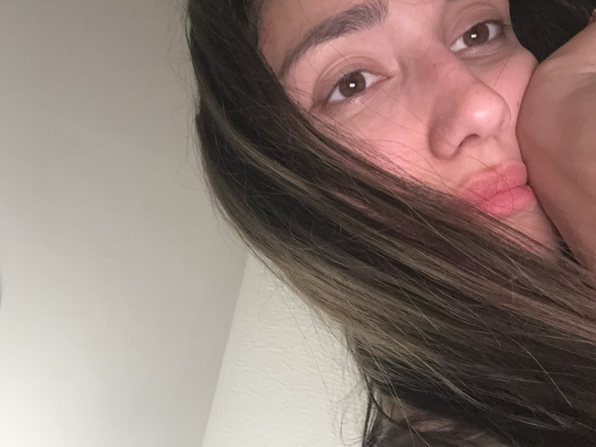 A close-up selfie shows a woman with brown hair and brown eyes. Part of her face is obscured by her hair and the edge of a hand/arm is pressed against her cheek. The background is a plain white wall. There is no information available to determine a location in the city of Zankovići, Montenegro.