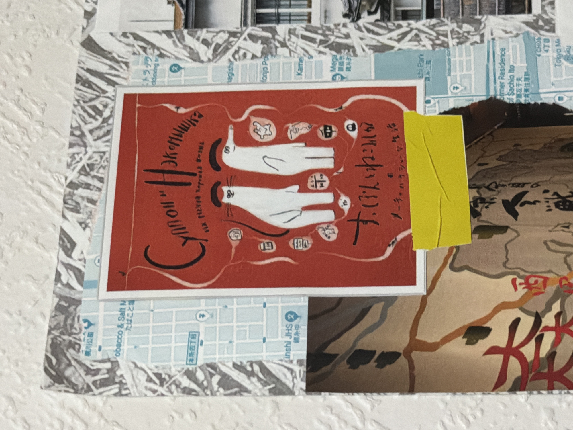 The image displays a collage of various papers and images affixed to a textured, off-white wall. The central element is a vibrant red poster featuring two cartoonish white animals, one resembling a cat and the other a more abstract creature with a long snout, rendered in a simple, outlined style. The poster has stylized black lettering across the top in a cursive font, and smaller text below the animals. A bright yellow piece of tape is affixed to the bottom portion of the red poster, partially obscuring some of the text.
Surrounding the central poster are fragments of what appear to be maps, with grids and blue lines indicating streets or areas. Some text on these map fragments is visible, including English words like "obacco & Salt", "Kinshi JHS", "Former Residence", and "Tokyo Ma". Other areas of the collage include abstract or patterned paper with black and gray strokes. To the right of the central poster, a portion of a building with windows is visible, suggesting an urban environment.
The overall impression is one of a layered, curated display, possibly in a home or a community space. The presence of the Russian text on the central poster, combined with the English text on the map fragments, hints at a location with a connection to both cultures, but no specific landmarks definitively place it within Moscow, Russia. The collage appears to be a personal arrangement of printed materials.