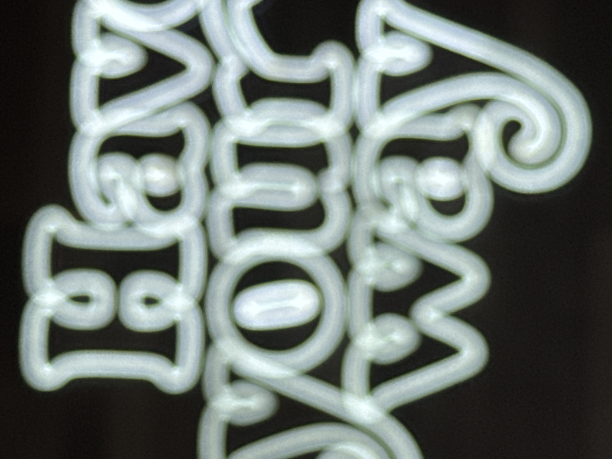 The media file displays white, illuminated text against a dark background, suggestive of a neon sign or light painting. The text is stylized and ornate, forming abstract shapes and curves rather than clearly defined letters. The overall impression is one of artistic expression or a decorative element rather than a literal depiction of a scene or event. There is no discernible indication of people, objects, or a specific setting, nor any details about time of day, weather, or emotions. The context of Karon, Thailand, is provided but not visually evident within the image itself.