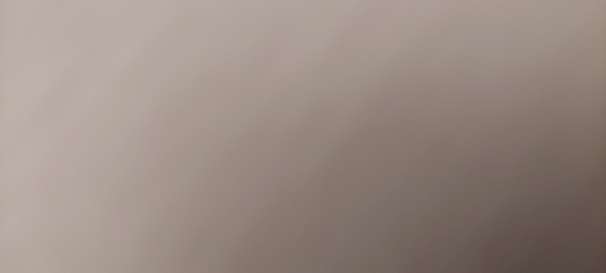 The image is a close-up, unfocused shot of a mottled surface, appearing to be a wall or fabric, with subtle variations in shade from light beige to a slightly darker taupe. There are no discernible features, objects, people, or actions visible. The scene is devoid of any environmental context that would suggest a specific location, including Bena-Yurt, Russia.